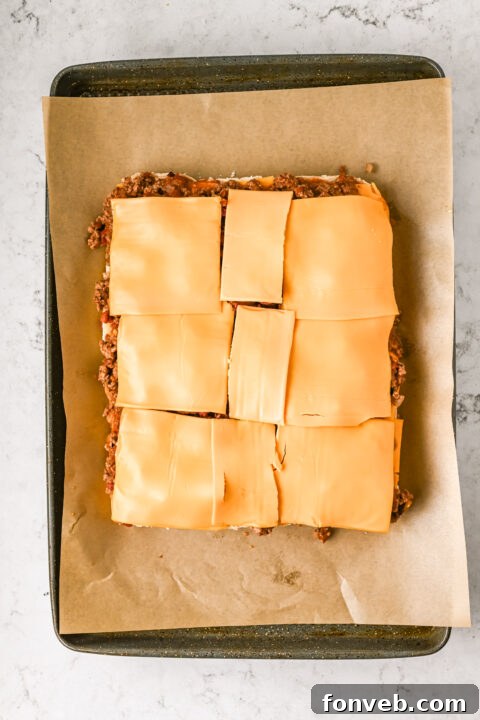The beef and bacon mixture being layered over cheese slices on the bottom slider buns.