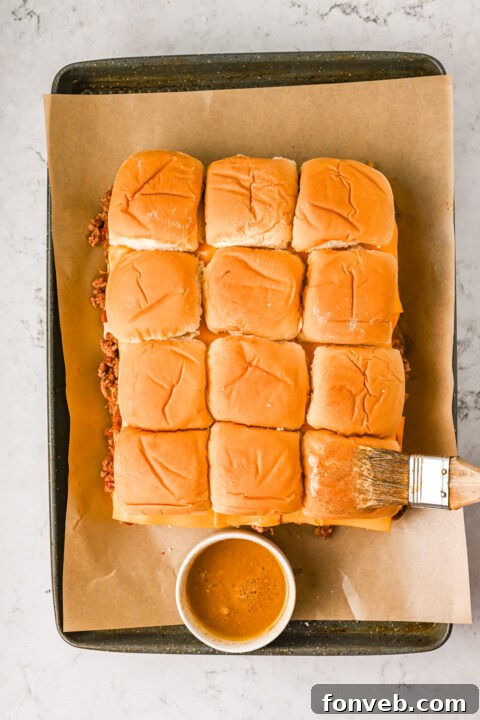 The assembled sliders in a baking pan, brushed with butter-dijon sauce and sprinkled with sesame seeds, ready for the oven.