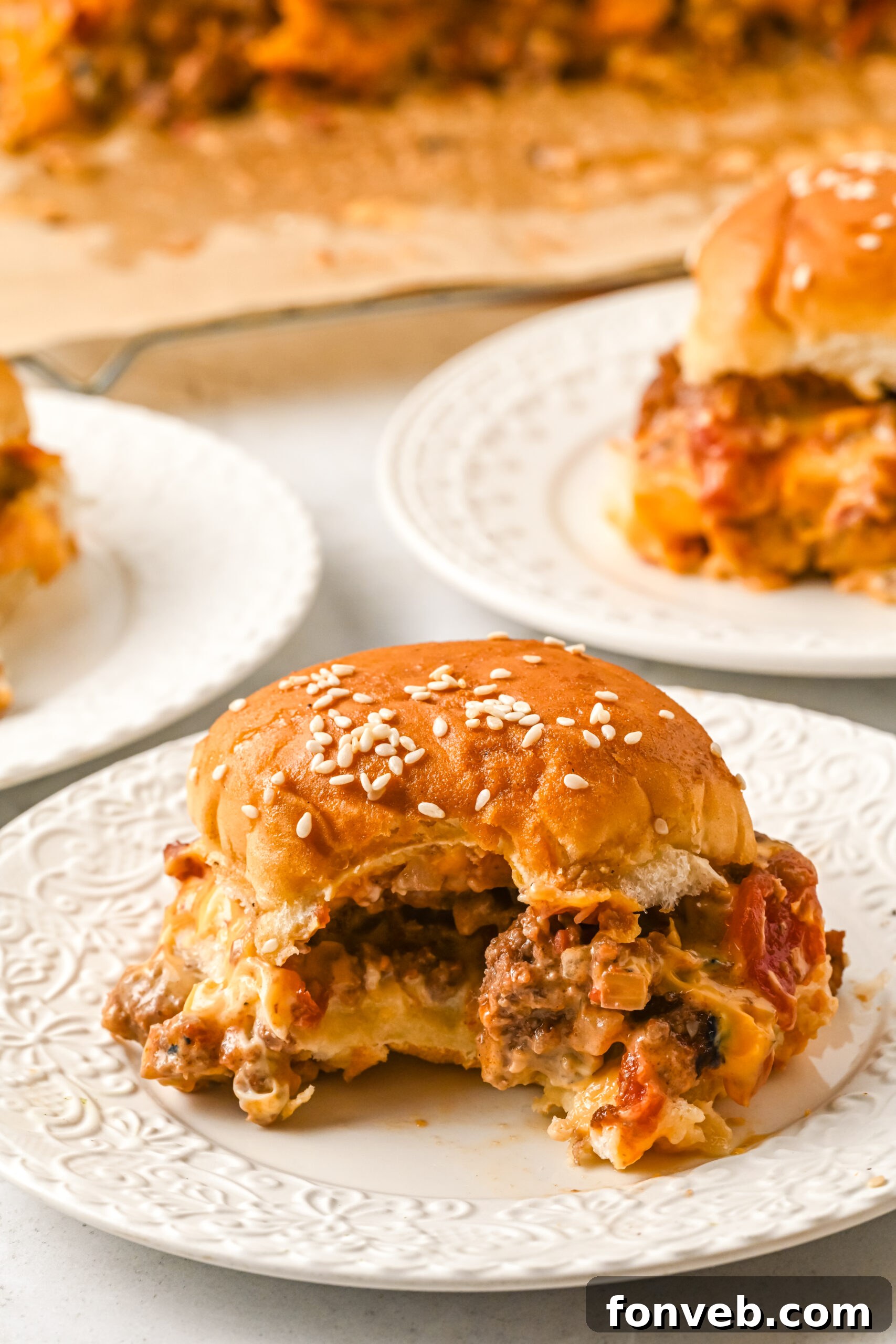 A close-up front view of a delicious cheeseburger slider on a white dish, with a bite playfully removed, revealing the juicy interior and melted cheese.