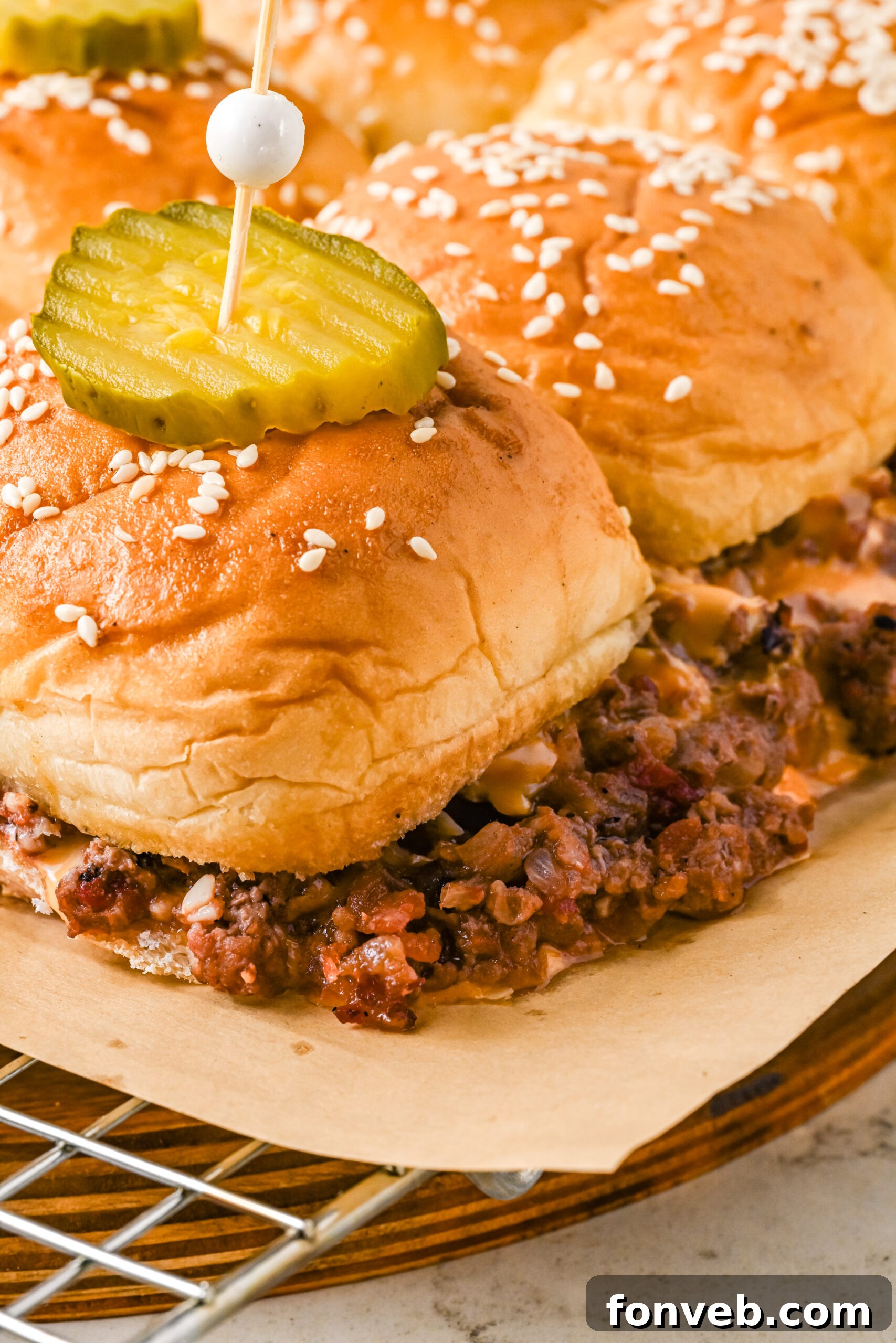 A close-up view of golden-brown cheeseburger sliders on a wire rack, topped with melted cheese and fresh pickle slices, emphasizing their juicy texture and irresistible appeal.