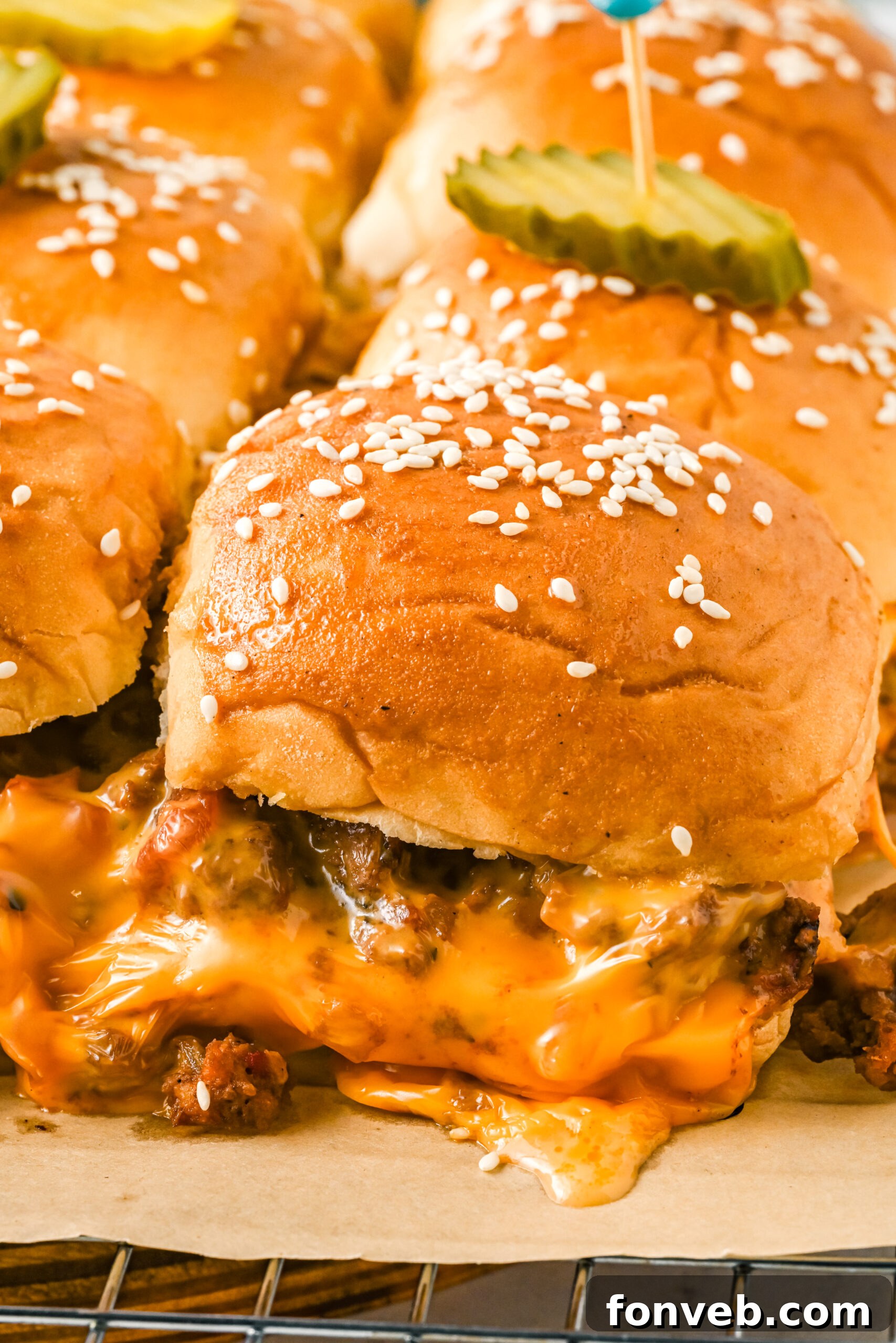 A close-up shot of several perfectly baked cheeseburger sliders arranged on a wire rack, with their golden-brown buns and visible layers of melted cheese and beef.