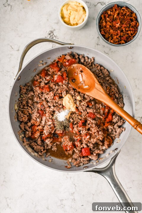 Ground beef cooking in a pan with sautéed onions, being broken apart with a spatula.