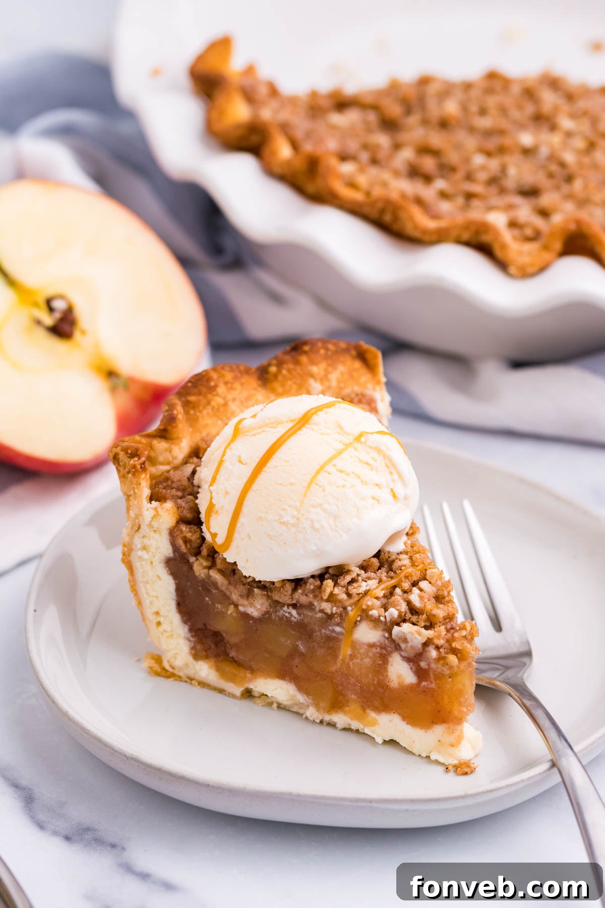Caramel Apple Crumble Cheesecake Pie 6 Front view of a slice of Apple Crumb Cheesecake Pie on a white dish with a scoop of vanilla ice cream.