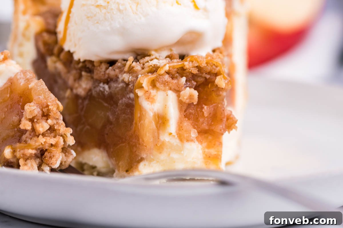 Caramel Apple Crumble Cheesecake Pie 8 Front view of a slice of Apple Crumb Cheesecake Pie on a white dish with a scoop of vanilla ice cream with a bite removed by a silver fork.