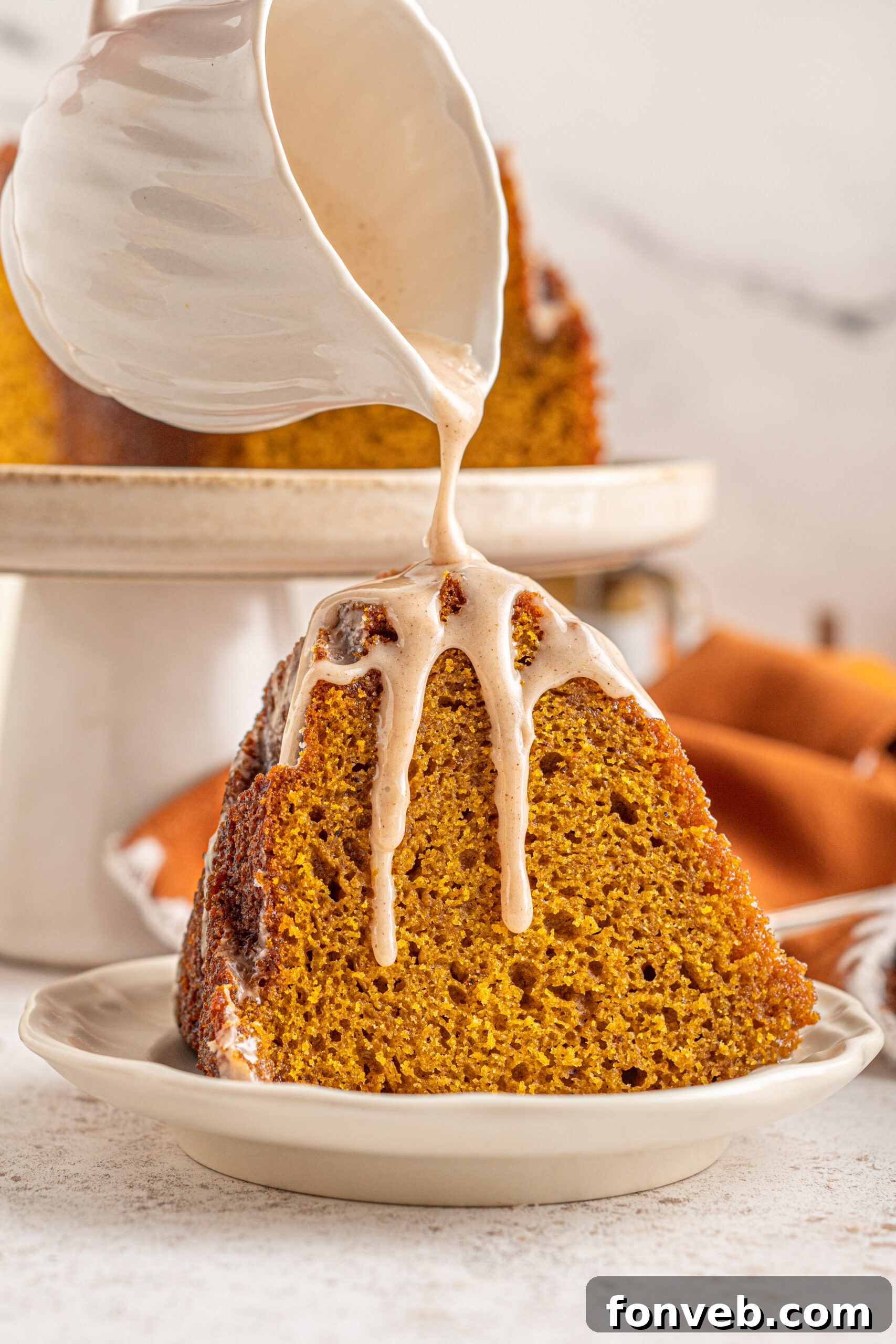 Harvest Pumpkin Bundt with Sweet Cinnamon Finish 12 A slice of Pumpkin Bundt Cake with Cinnamon Sugar Glaze on a white dish with glaze being poured over top.