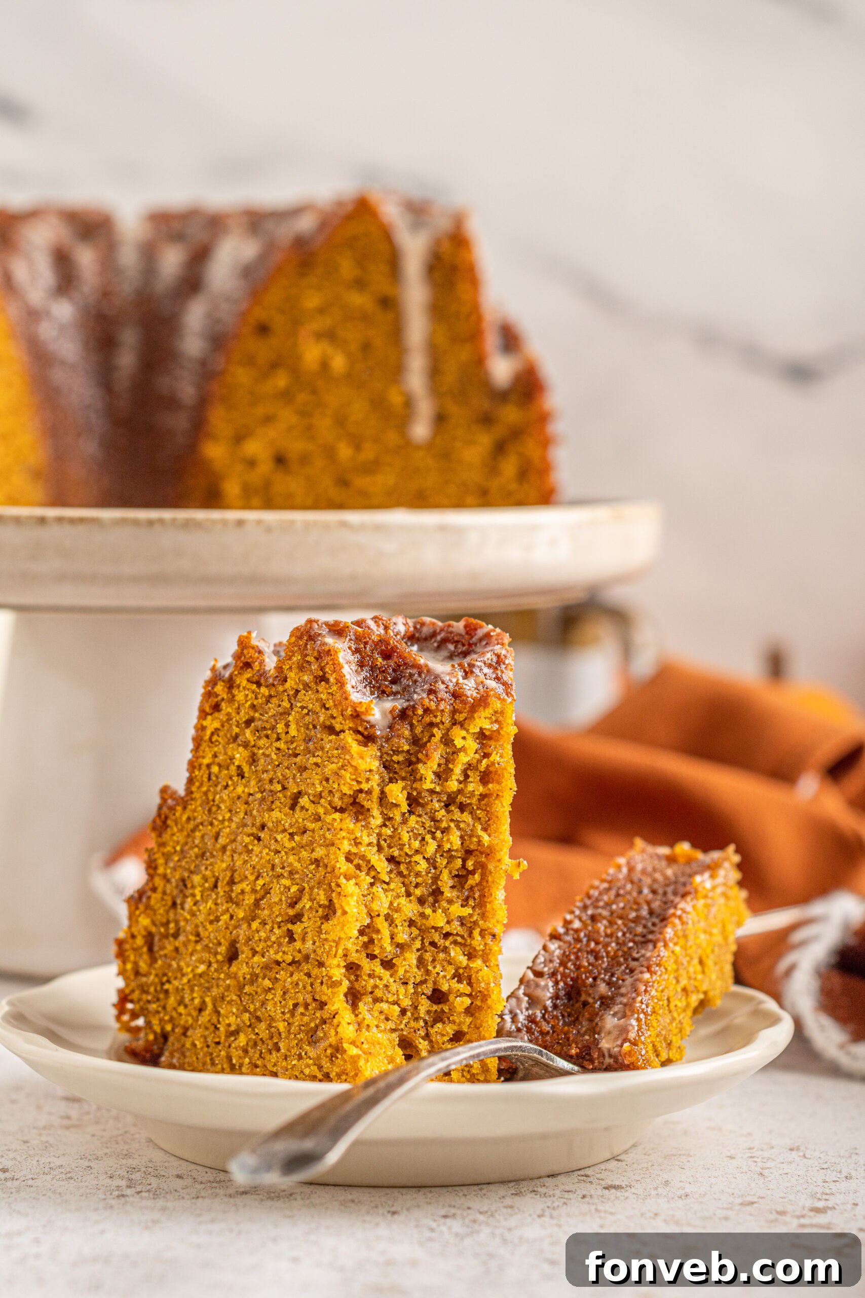 Harvest Pumpkin Bundt with Sweet Cinnamon Finish 14 Close-up of a slice of Pumpkin Bundt Cake with Cinnamon Sugar Glaze, a bite taken out with a silver fork, showing its moist texture.