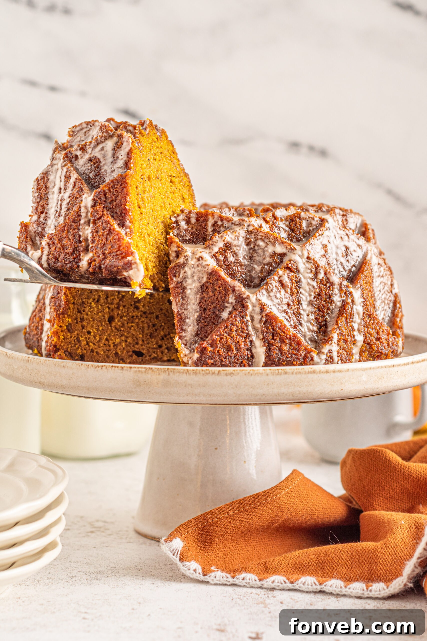 Harvest Pumpkin Bundt with Sweet Cinnamon Finish 5 A silver spatula delicately lifting a perfect slice of Pumpkin Bundt Cake with Cinnamon Sugar Glaze from the whole cake.