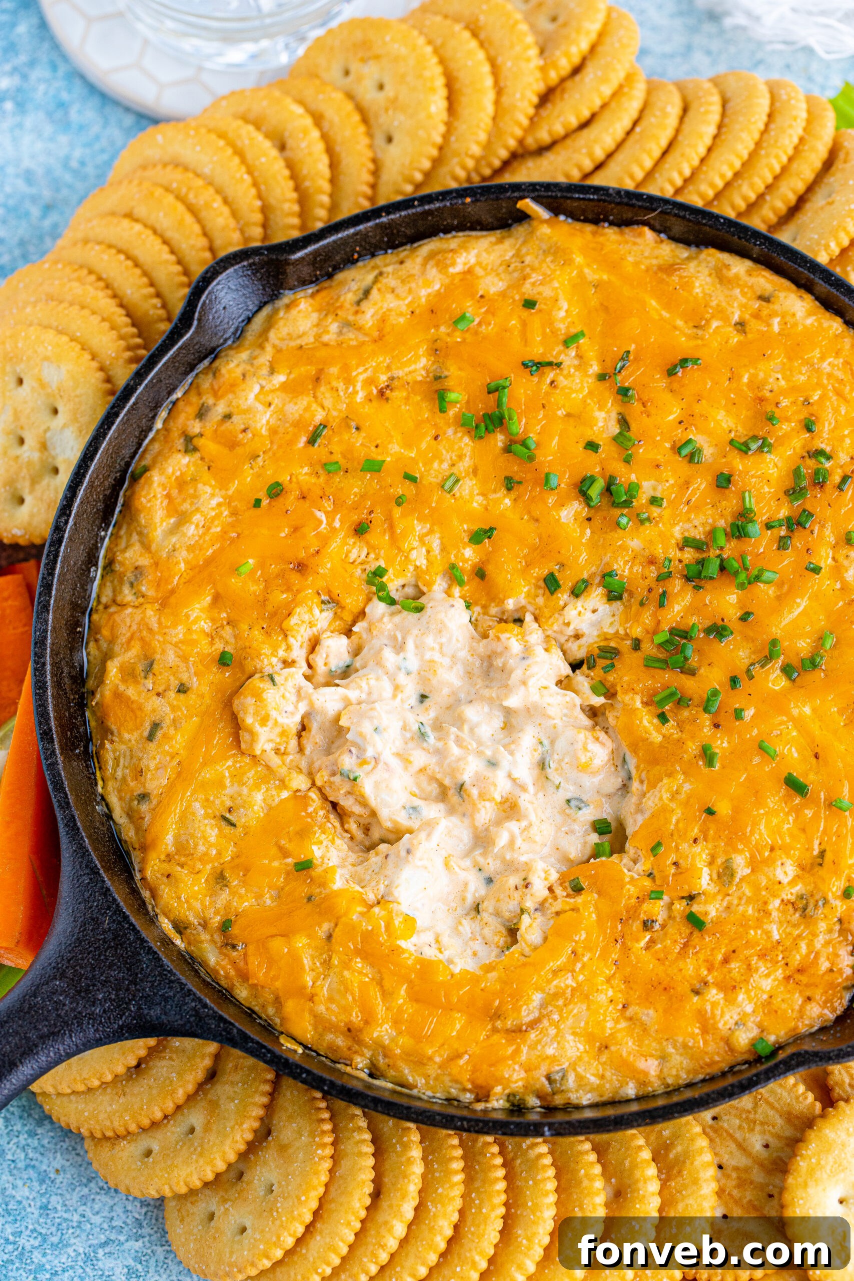 Overhead view of a perfectly baked Crab Dip in a cast iron skillet, surrounded by an assortment of crackers and colorful vegetable sticks.