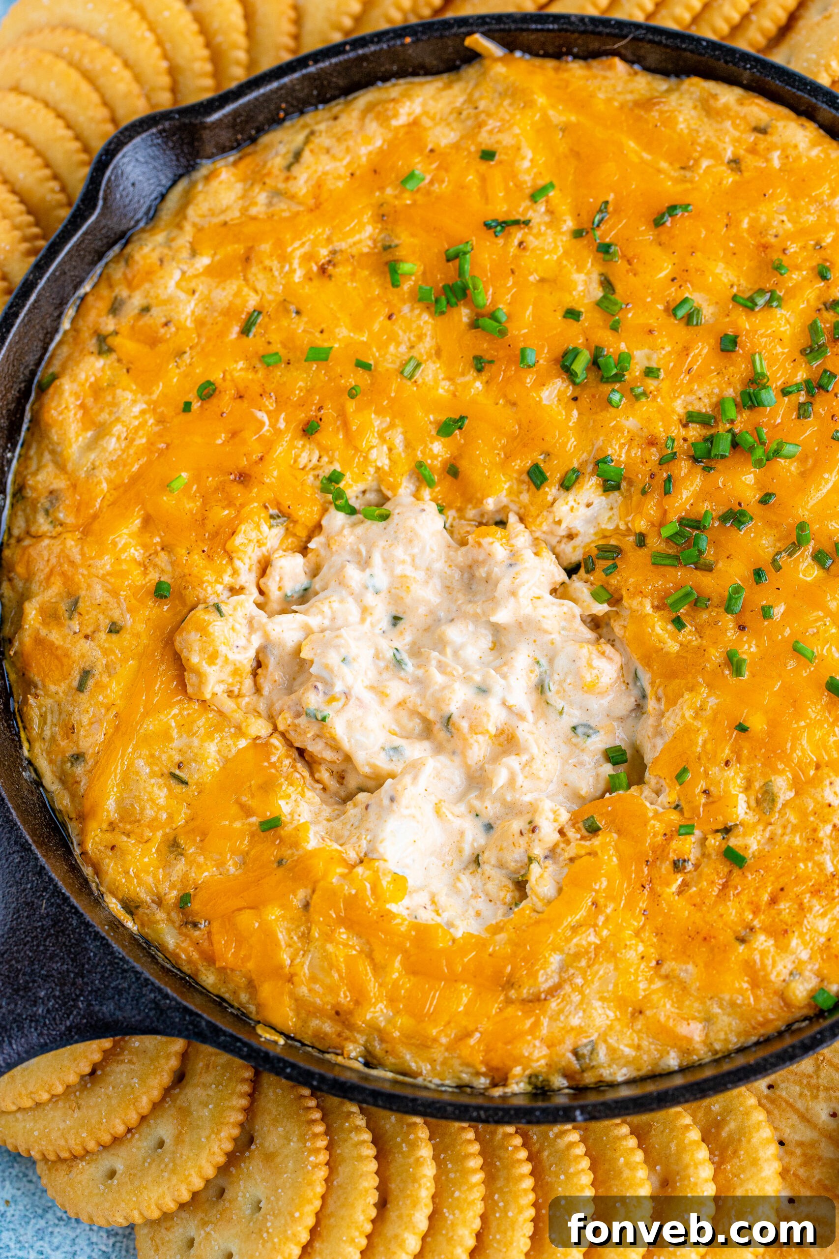 Overhead close-up of the finished Crab Dip in a cast iron skillet, garnished with fresh chives and served with crackers.
