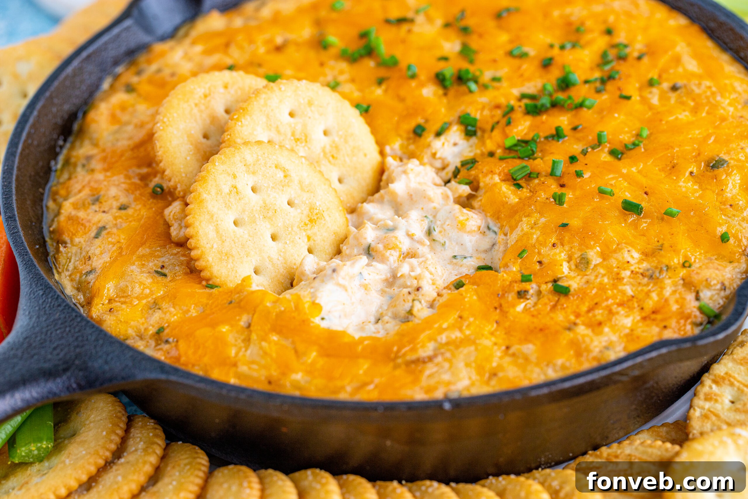 Front view of Creamy Crab Dip in a cast iron skillet, perfectly golden brown, served with a spread of crackers and fresh veggie sticks.