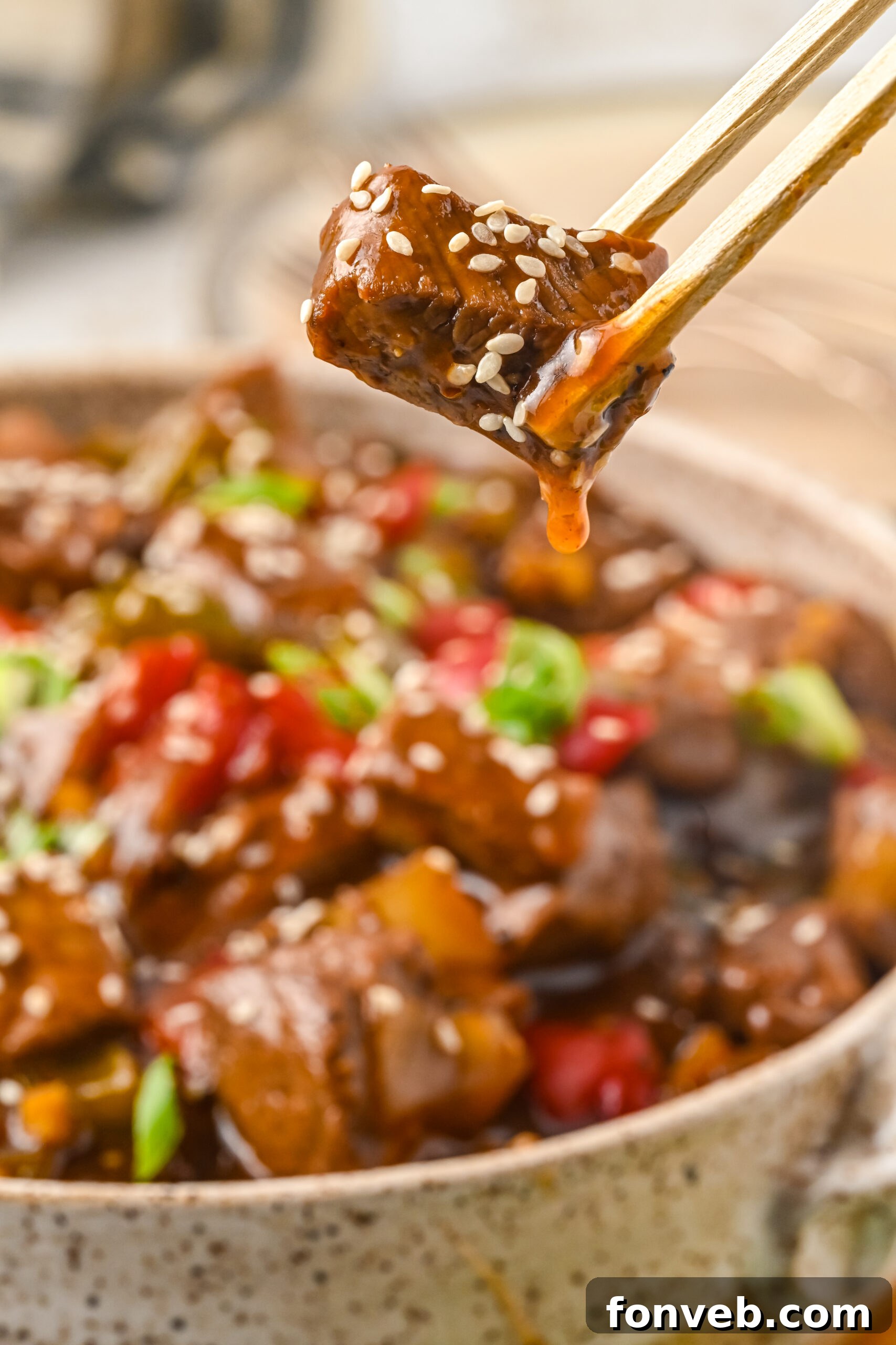 Close up view of chopsticks holding a piece of Chinese Pepper Steak.
