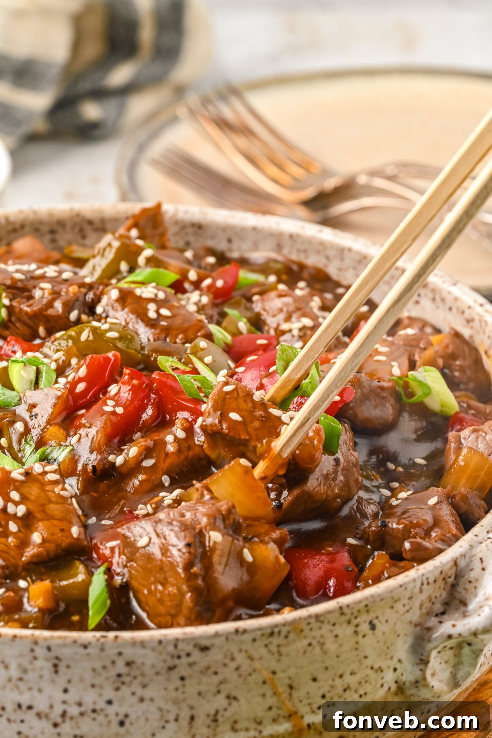 Close up view of chopsticks holding a piece of Chinese Pepper Steak.