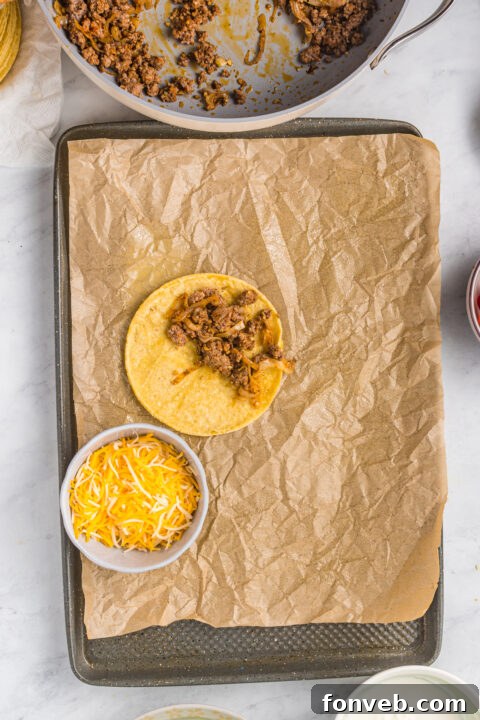 Golden Crispy Beef Tacos 14 Several partially folded and filled tacos arranged on a baking sheet, illustrating the back-to-back positioning to maintain their shape.