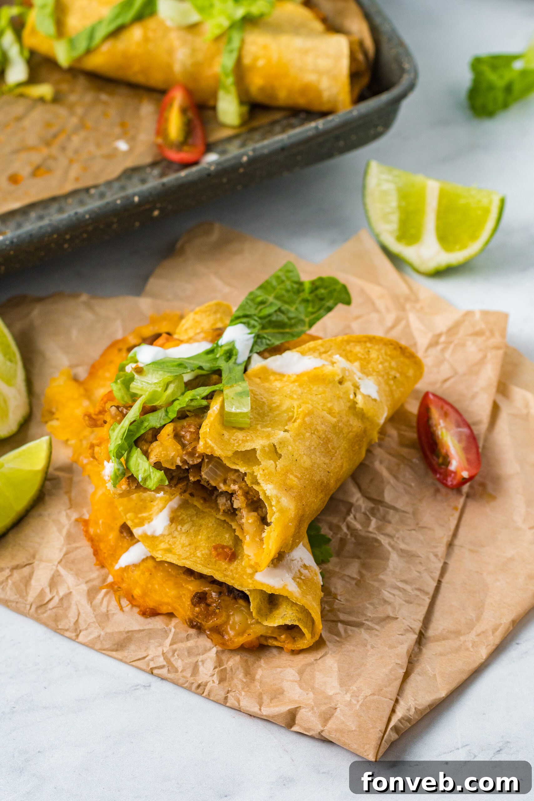 Golden Crispy Beef Tacos 18 Front view of two stacked Crispy Beef Tacos on parchment paper, with one taco having a bite removed, showcasing its crispy texture.