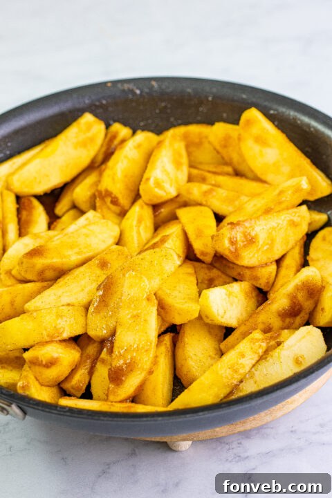 Apple slices being coated in melted butter, sugar, and cinnamon in the skillet.