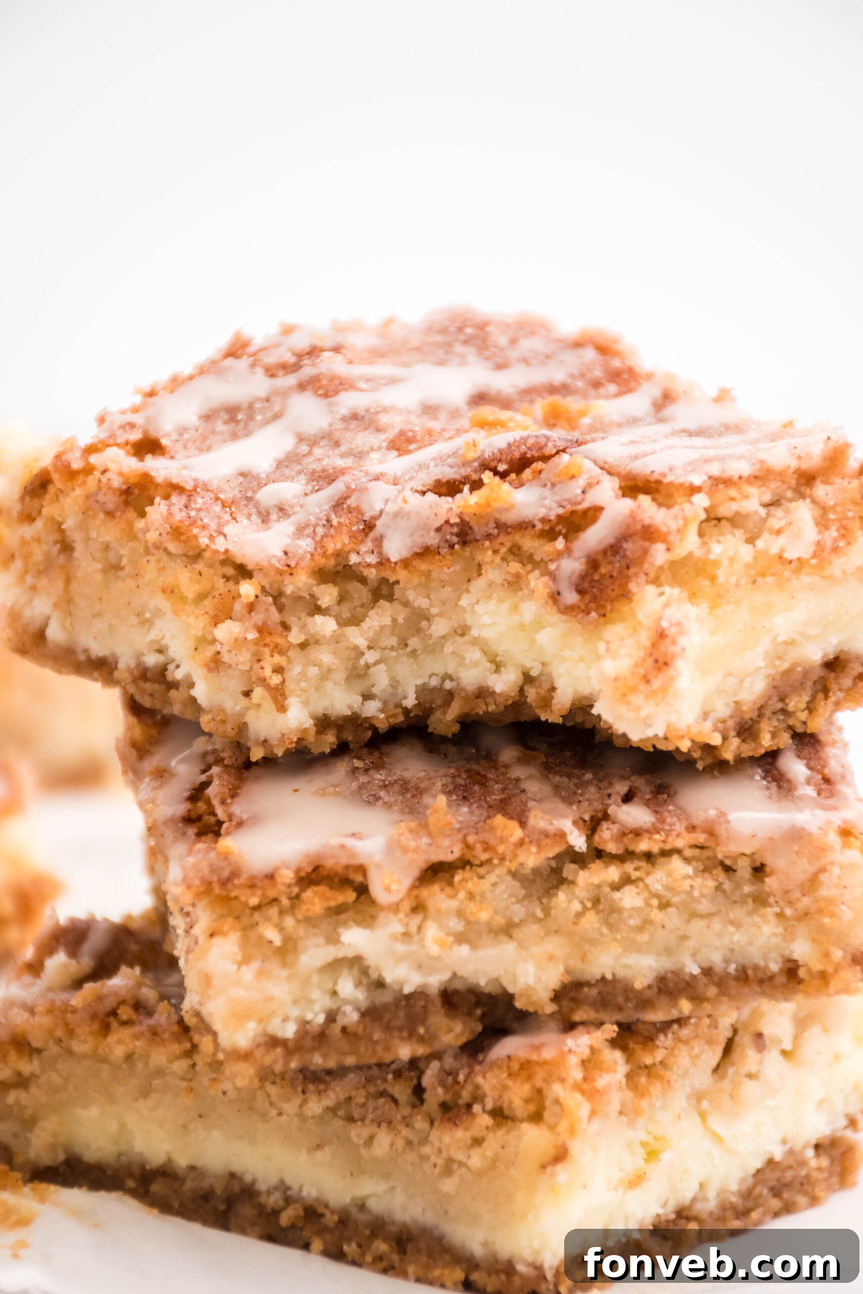 Front view of three Snickerdoodle Cheesecake Bars stacked with a bite removed from the top bar, showcasing the creamy filling and spiced cookie layer.