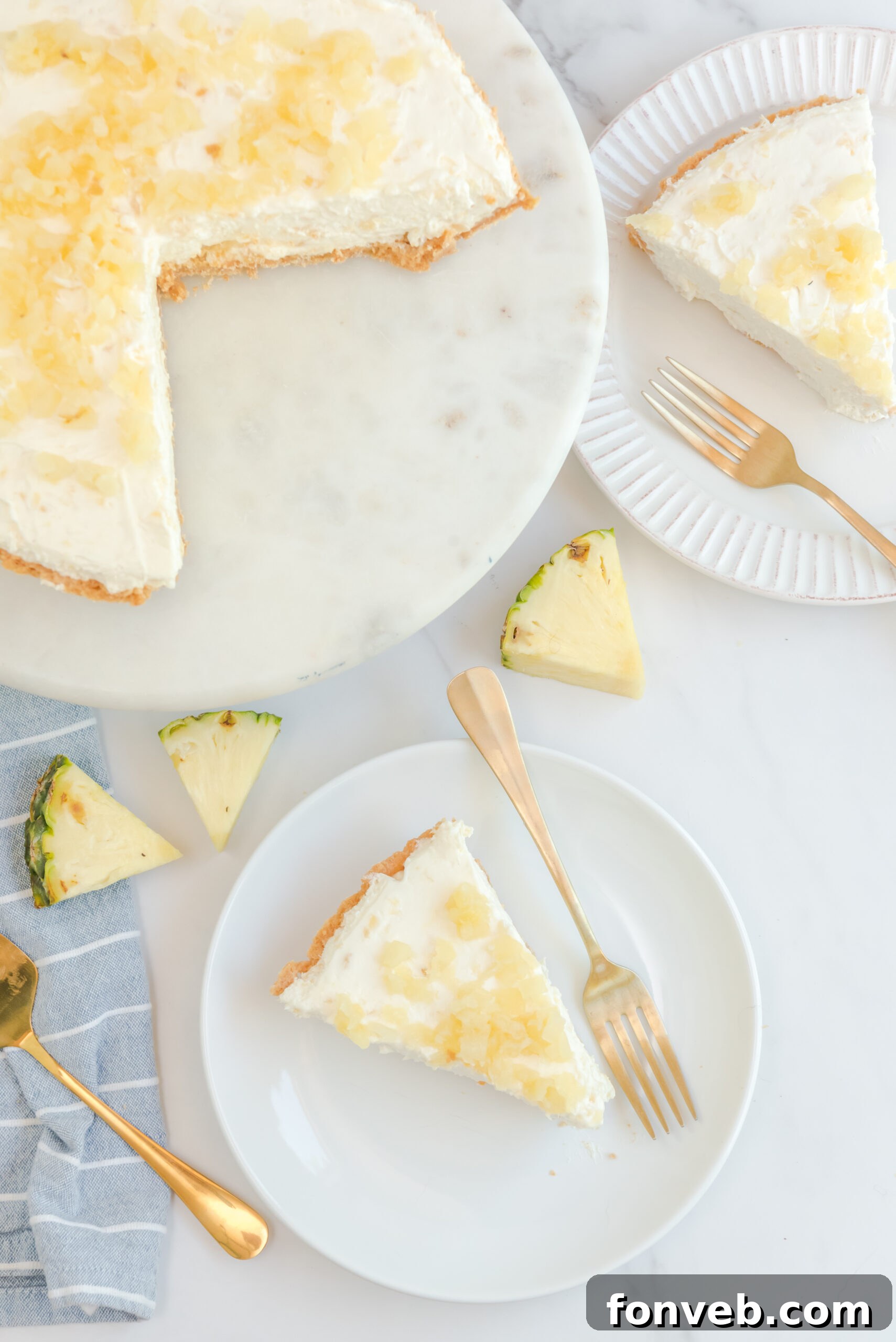 Overhead view of No Bake Pineapple Cheesecake with two slices removed and served on a white plate with gold forks.