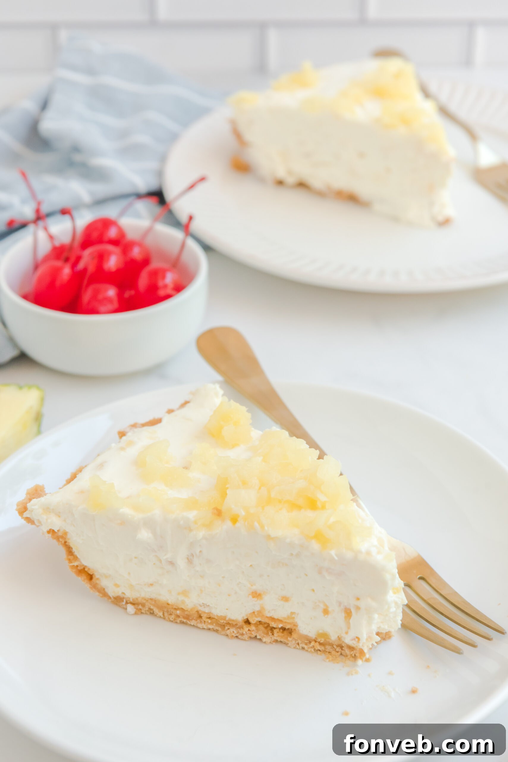 Side view of a slice of No Bake Pineapple Cheesecake served on a white plate with a gold fork.