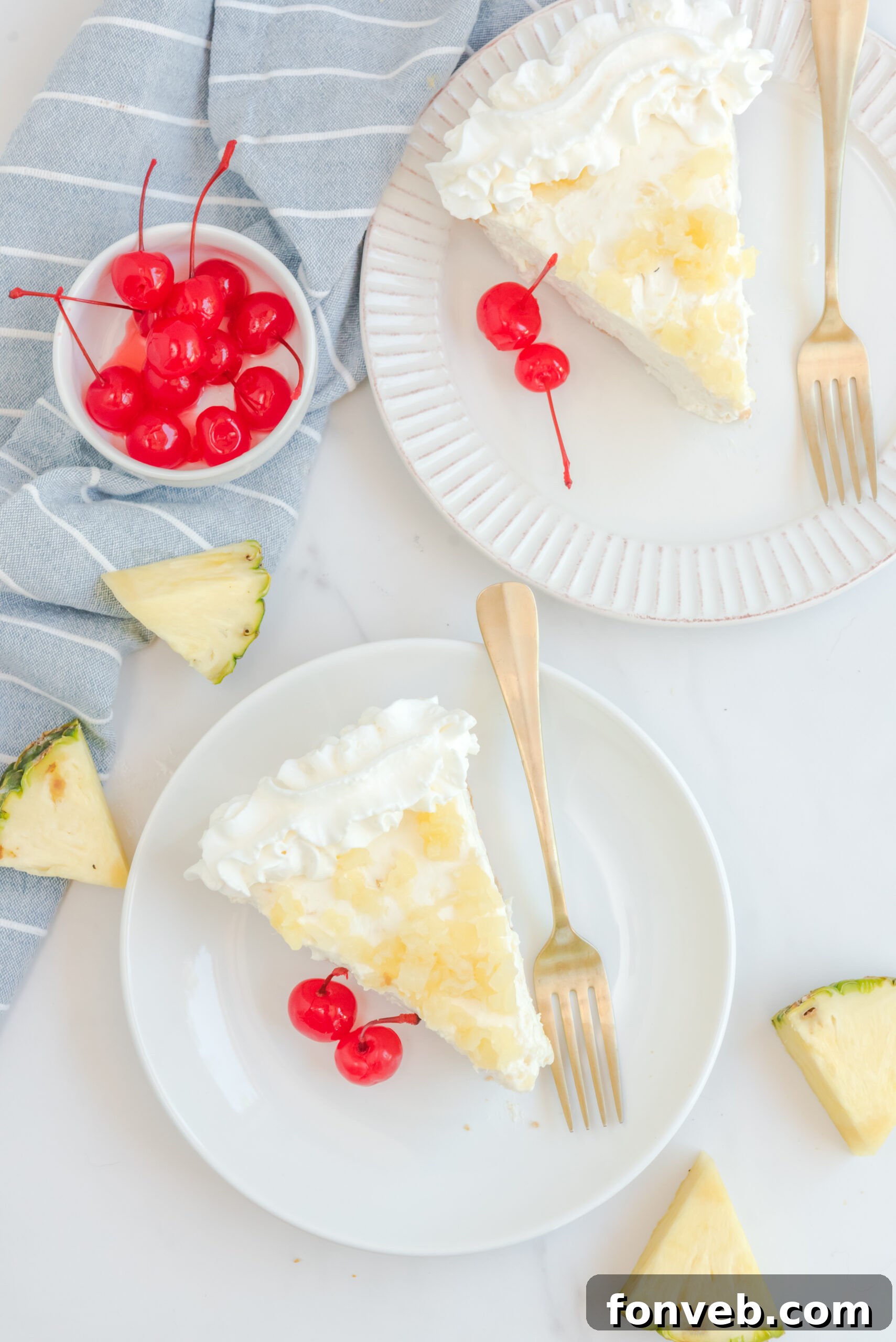 Overhead view of two slices of No Bake Pineapple Cheesecake served on white plates with gold forks.