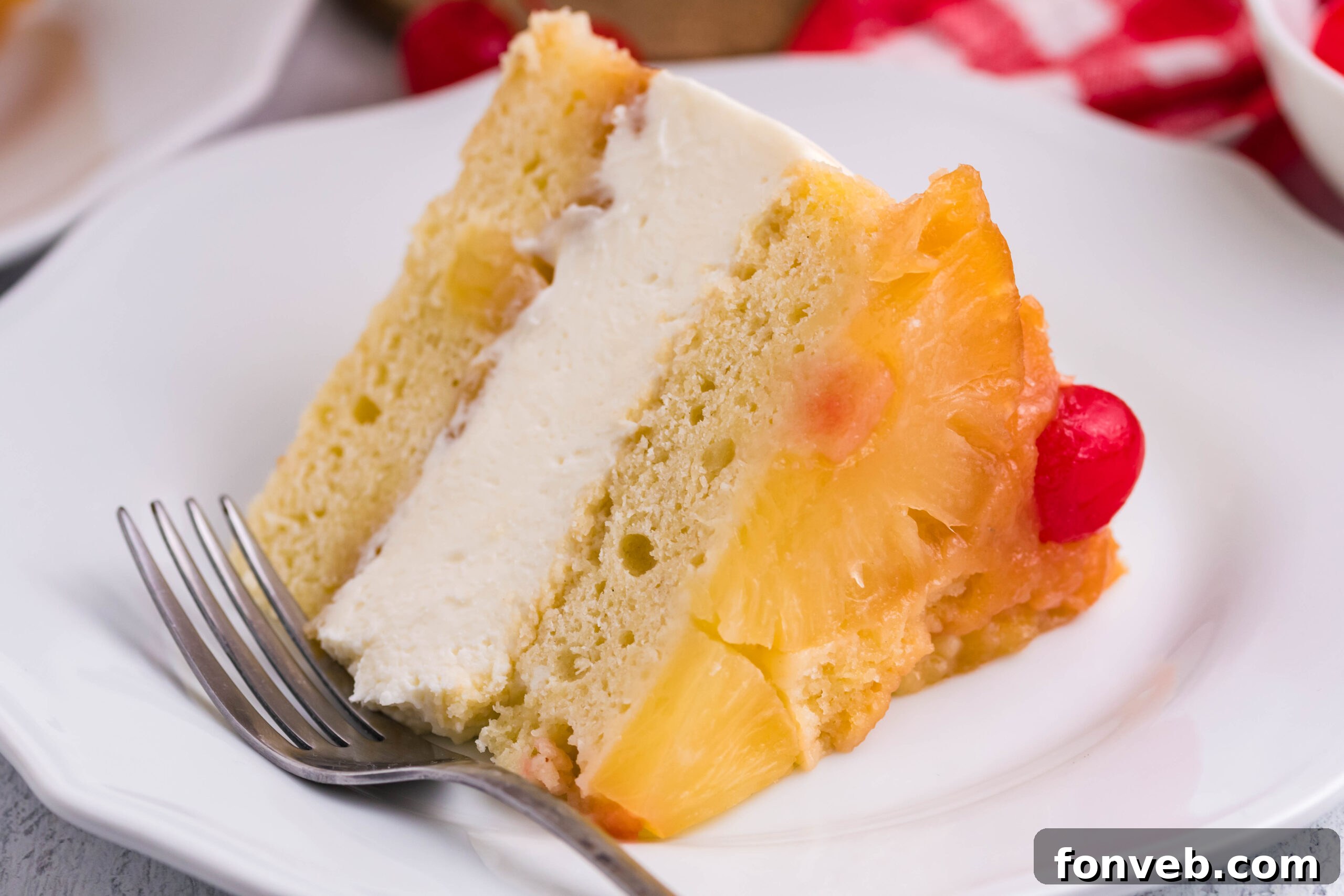 Front view of a slice of Pineapple Upside Down Cheesecake Cake served on a white plate with a silver fork.