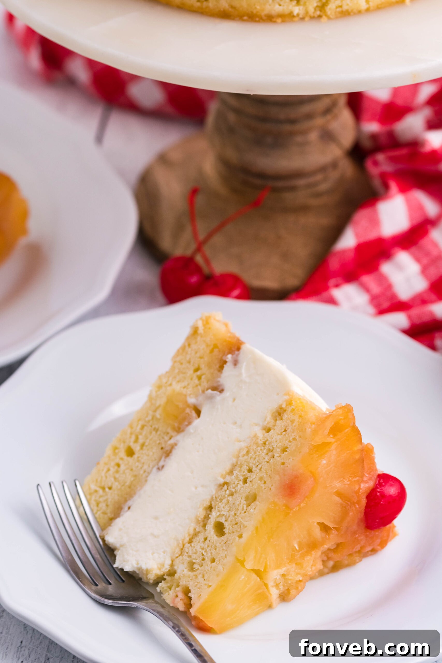 Front view of a slice of Pineapple Upside Down Cheesecake Cake served on a white plate with a silver fork.
