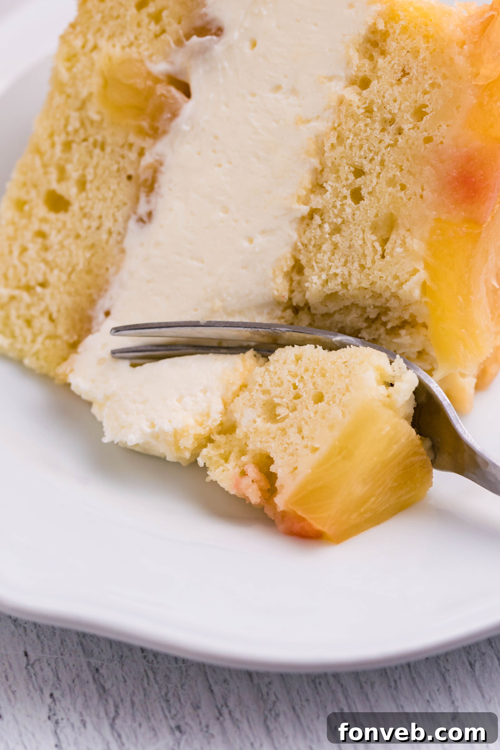 Up close view of a silver fork removing a bite from a slice of Pineapple Upside Down Cheesecake Cake.