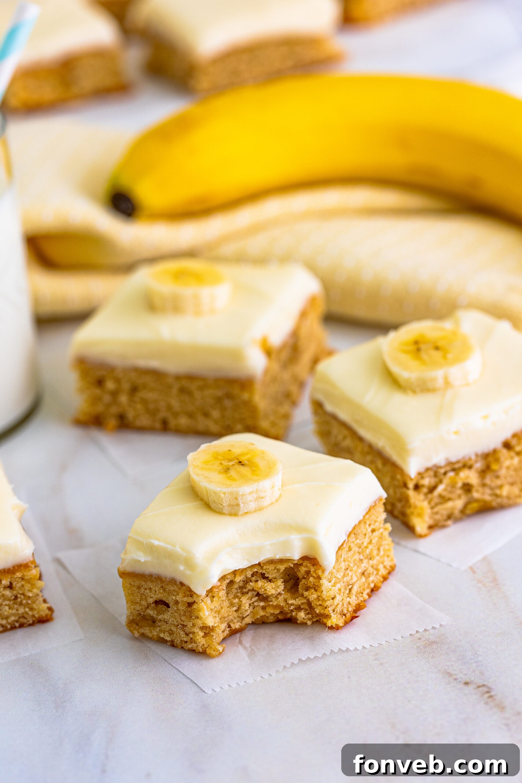 Front view of Banana Brownies on parchment paper with a corner brownie having a bite removed, showcasing the frosting.
