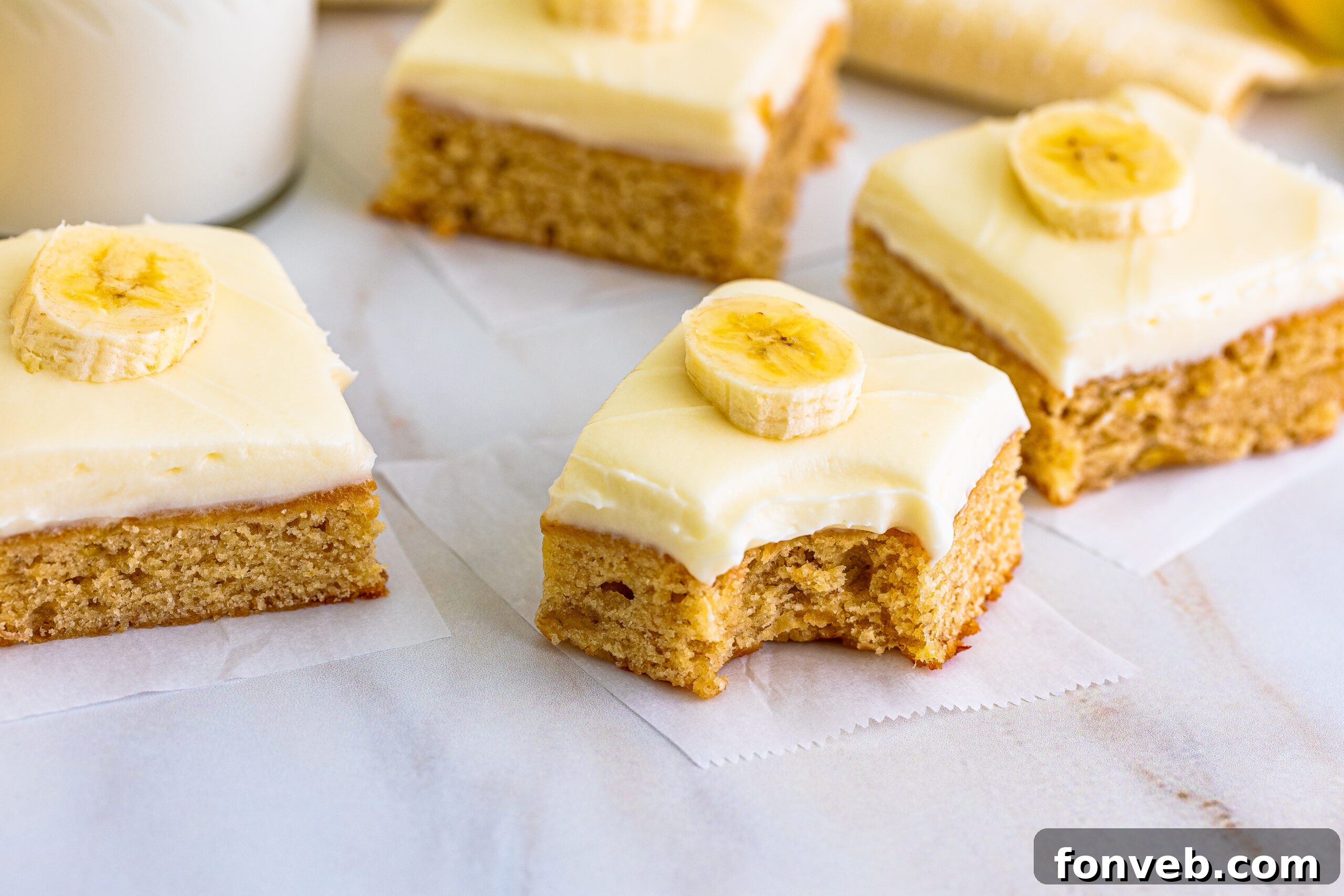 Front view of Banana Brownies on parchment paper with one brownie featuring a bite, highlighting its soft texture and golden hue.