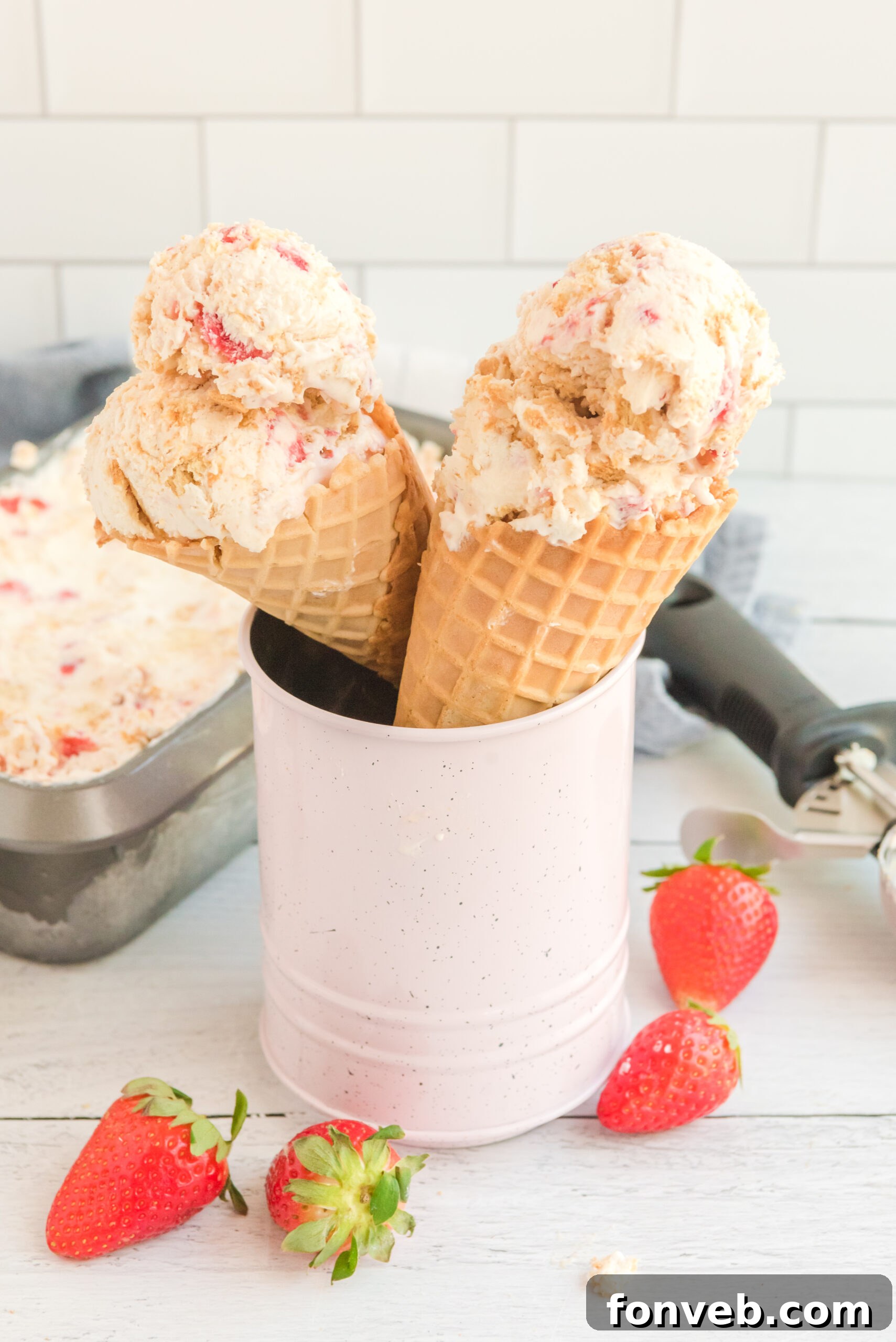 Frozen Strawberry Cheesecake Dream 6 Front view of two waffle cones with a scoop of Strawberry Cheesecake Ice Cream in each cone.