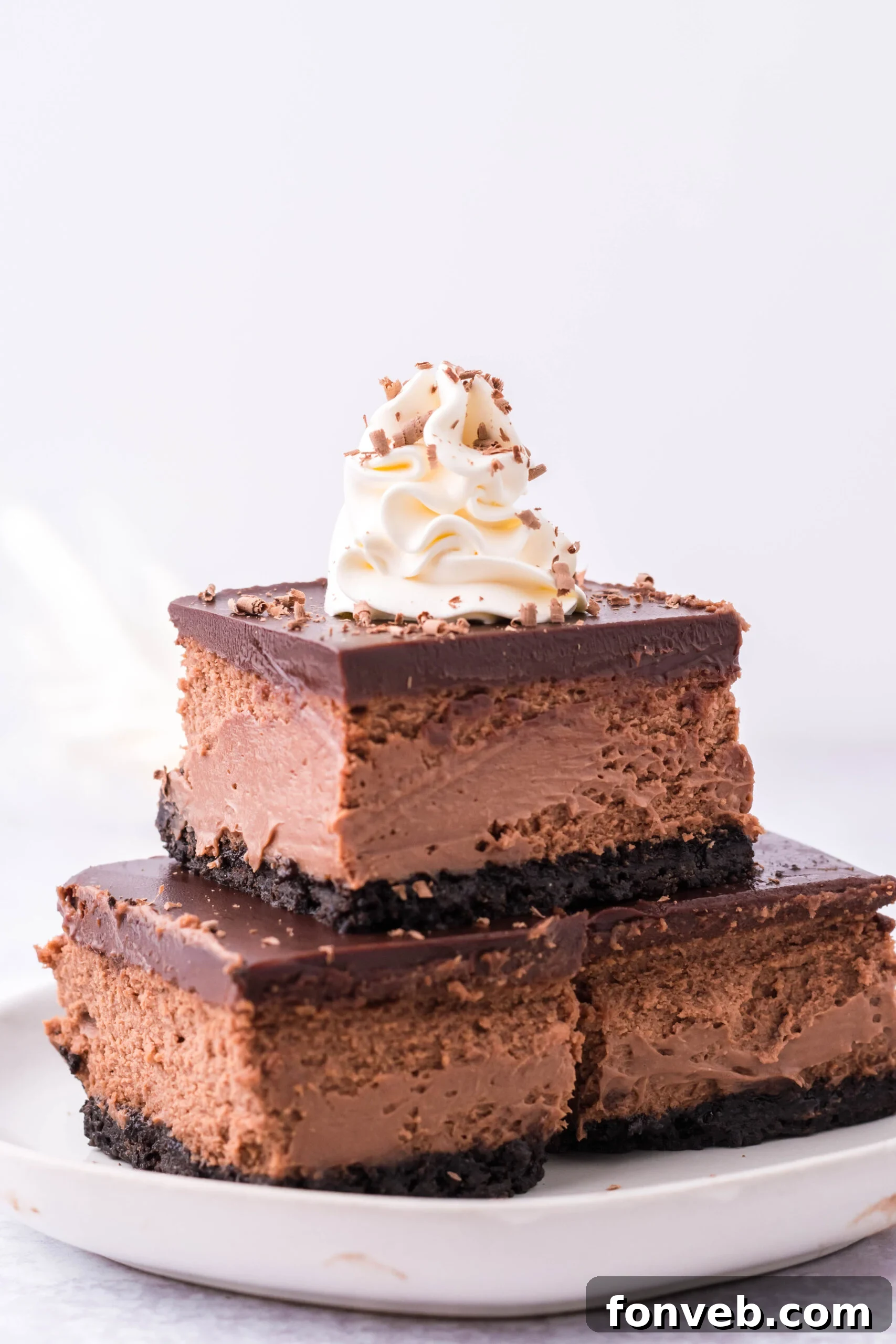 Three Chocolate Cheesecake bars topped on top of each other topped with whipped cream and chocolate shavings.