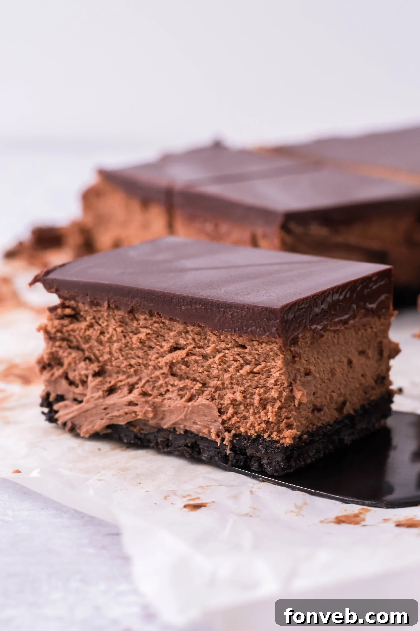 A bar of chocolate cheesecake being removed with a black spatula.