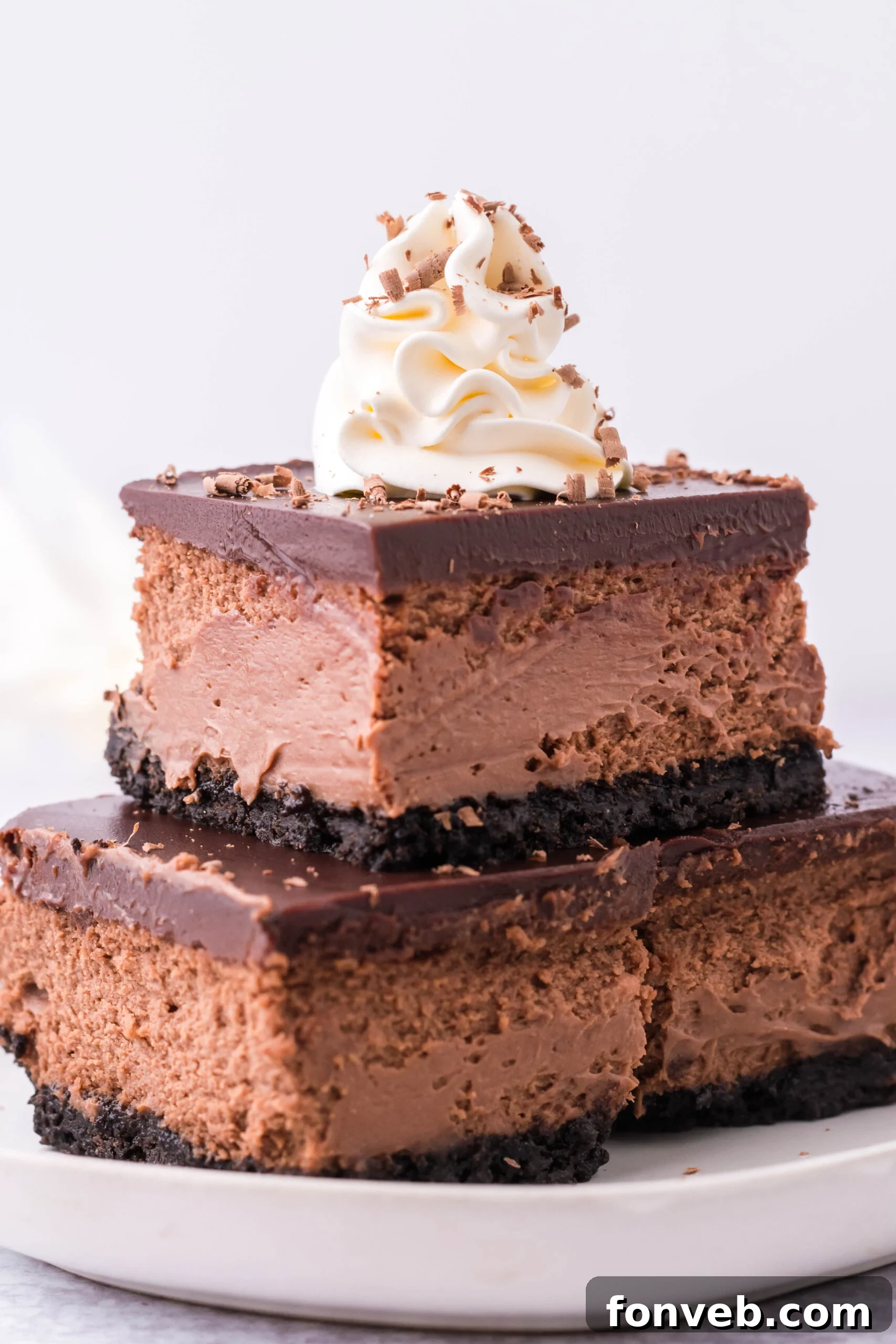 Three Chocolate Cheesecake bars topped on top of each other topped with whipped cream and chocolate shavings.