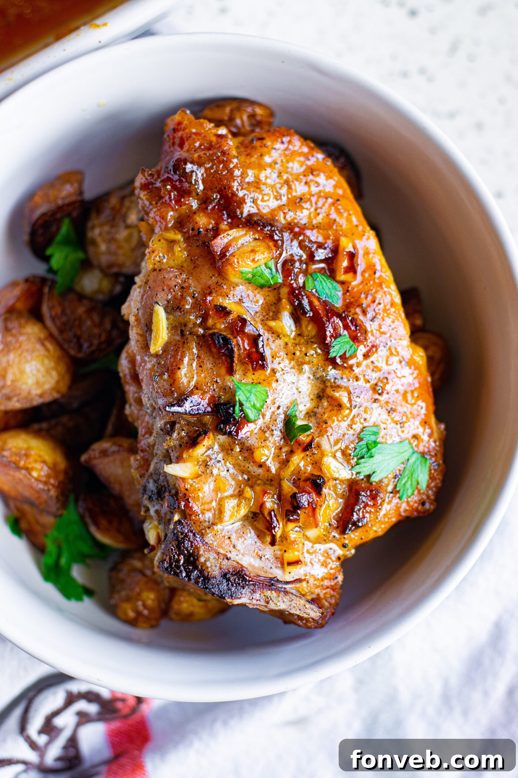Overhead view of a plated Honey Garlic Pork Chop served over a bed of roasted potatoes, garnished with fresh herbs.