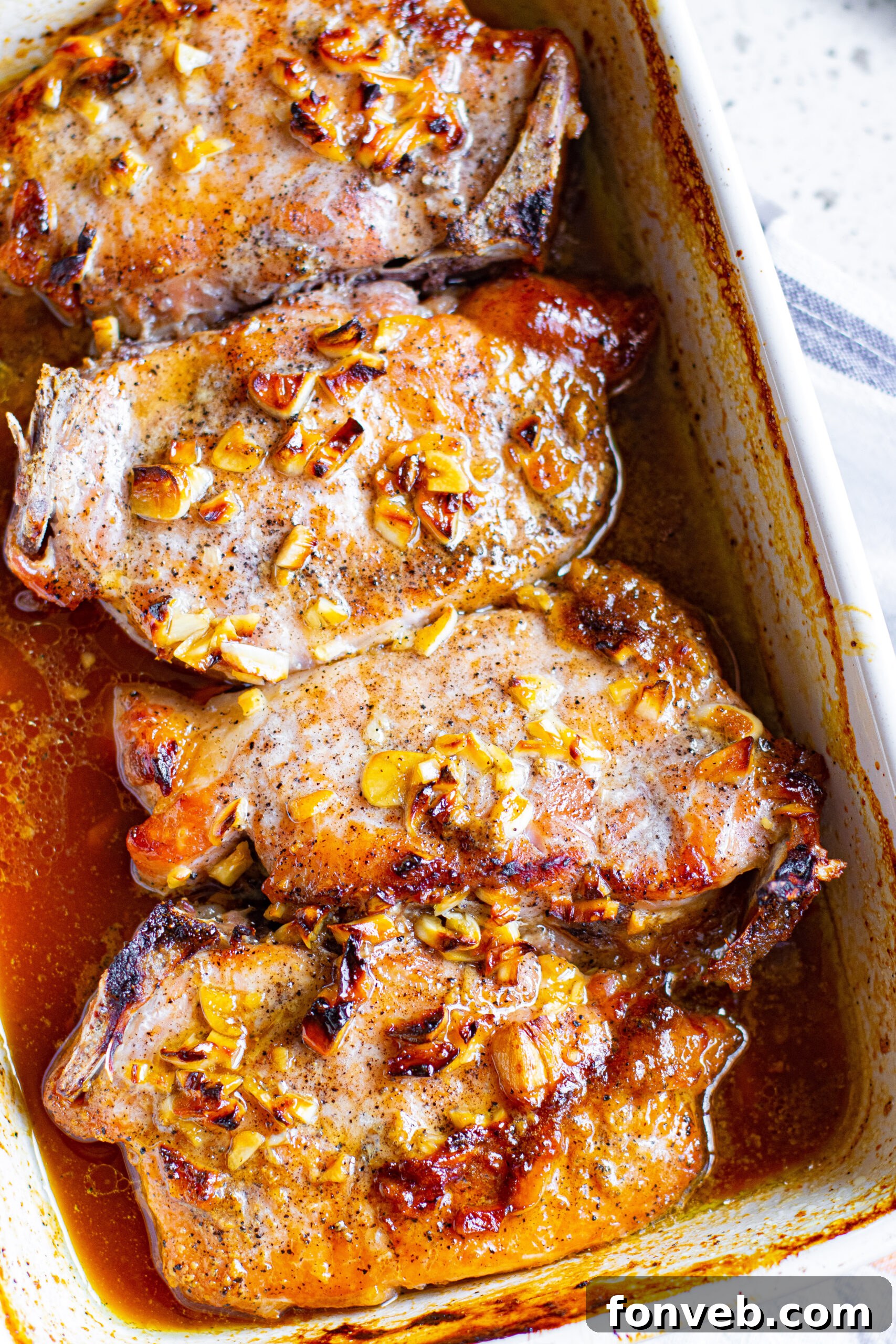 Close up view of succulent Honey Garlic Pork Chops simmering in a white baking dish.