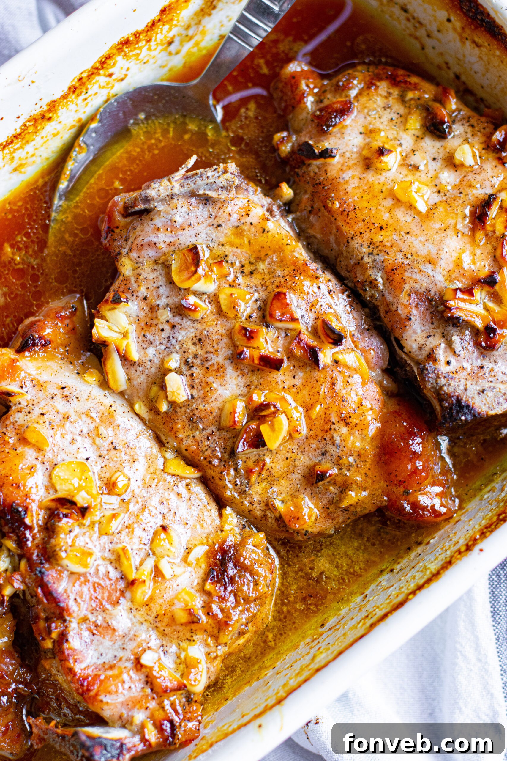 Close up shot of glistening Honey Garlic Pork Chops baked in a white ceramic dish.