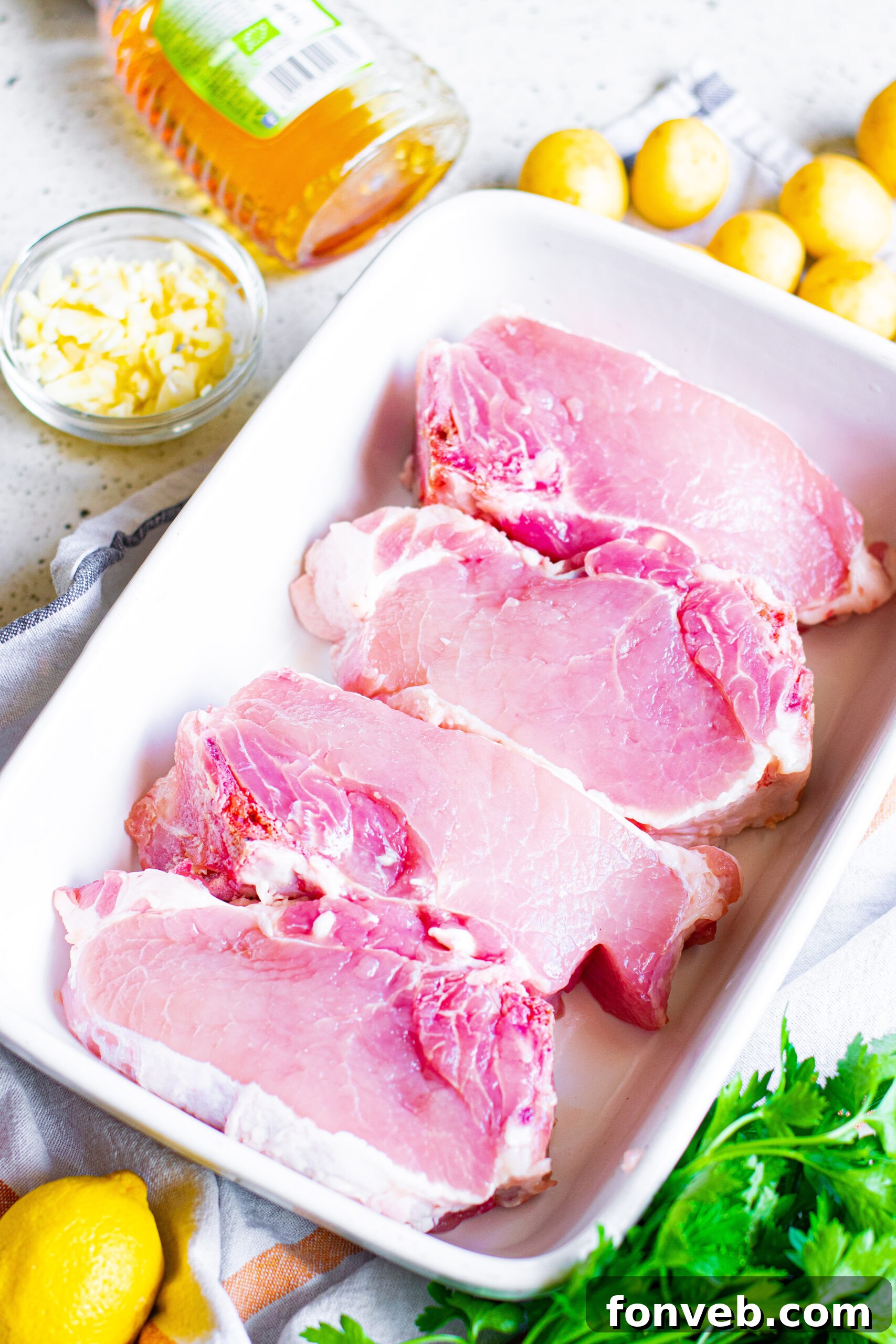 Overhead view of fresh ingredients laid out for Honey Garlic Pork Chops: pork chops, garlic, honey, lemon, butter, salt, pepper.