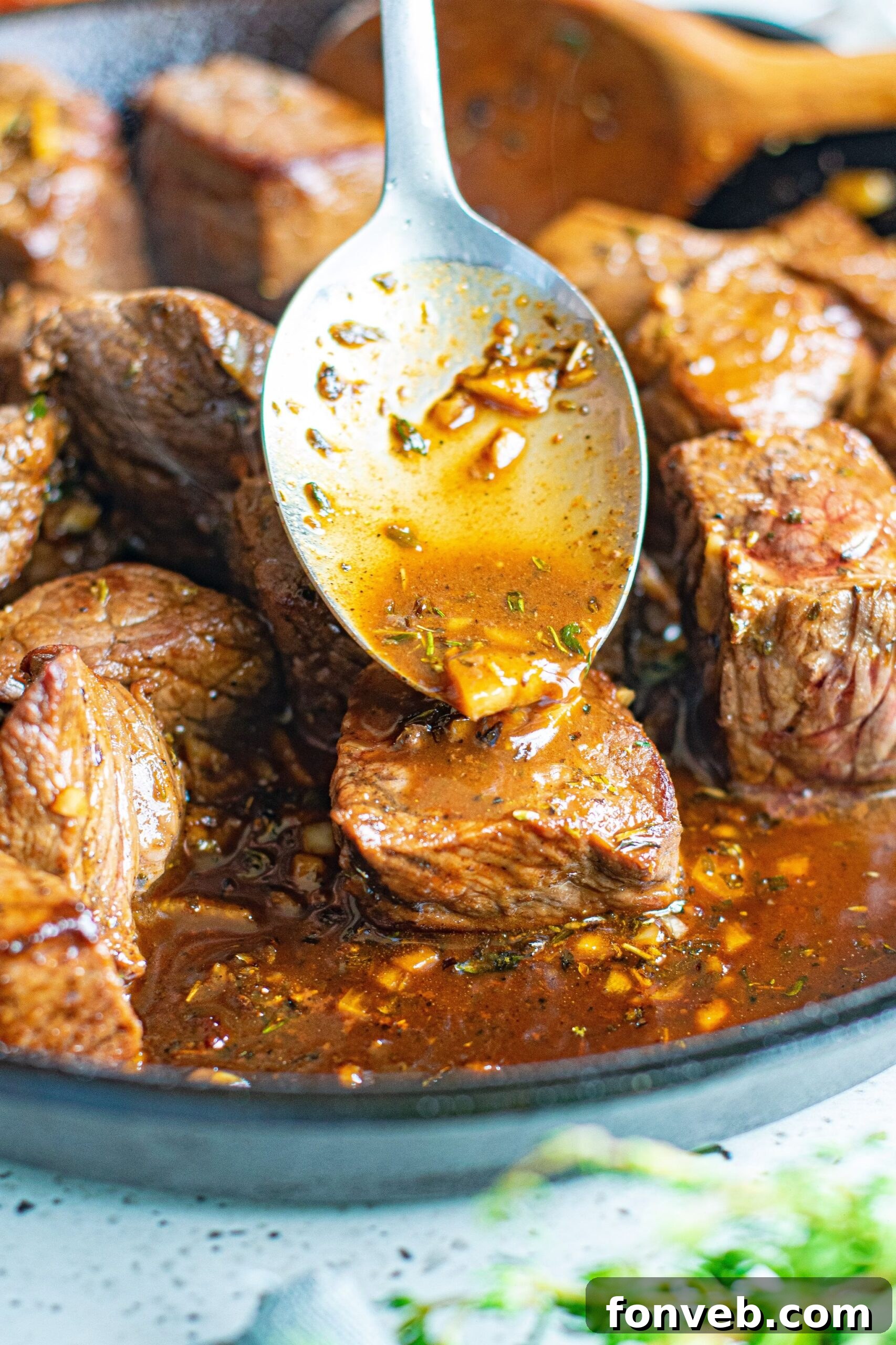Close up view of a silver spoon spooning the garlic honey sauce on to the Garlic Honey Steak Bites.