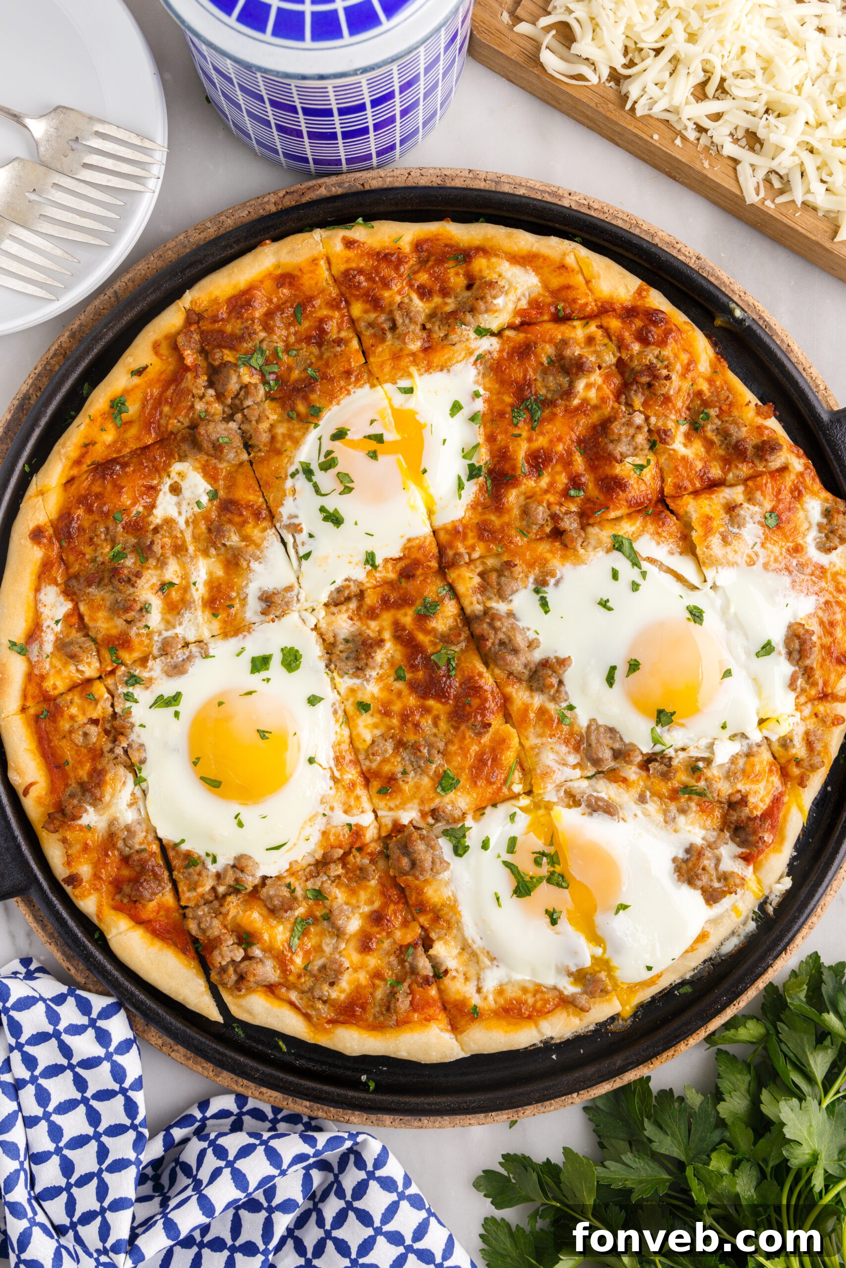 A vibrant, freshly baked Breakfast Pizza, generously topped with scrambled eggs, cooked sausage, melted mozzarella, and fresh herbs, presented on a sleek black pizza pan and sliced into perfect squares.