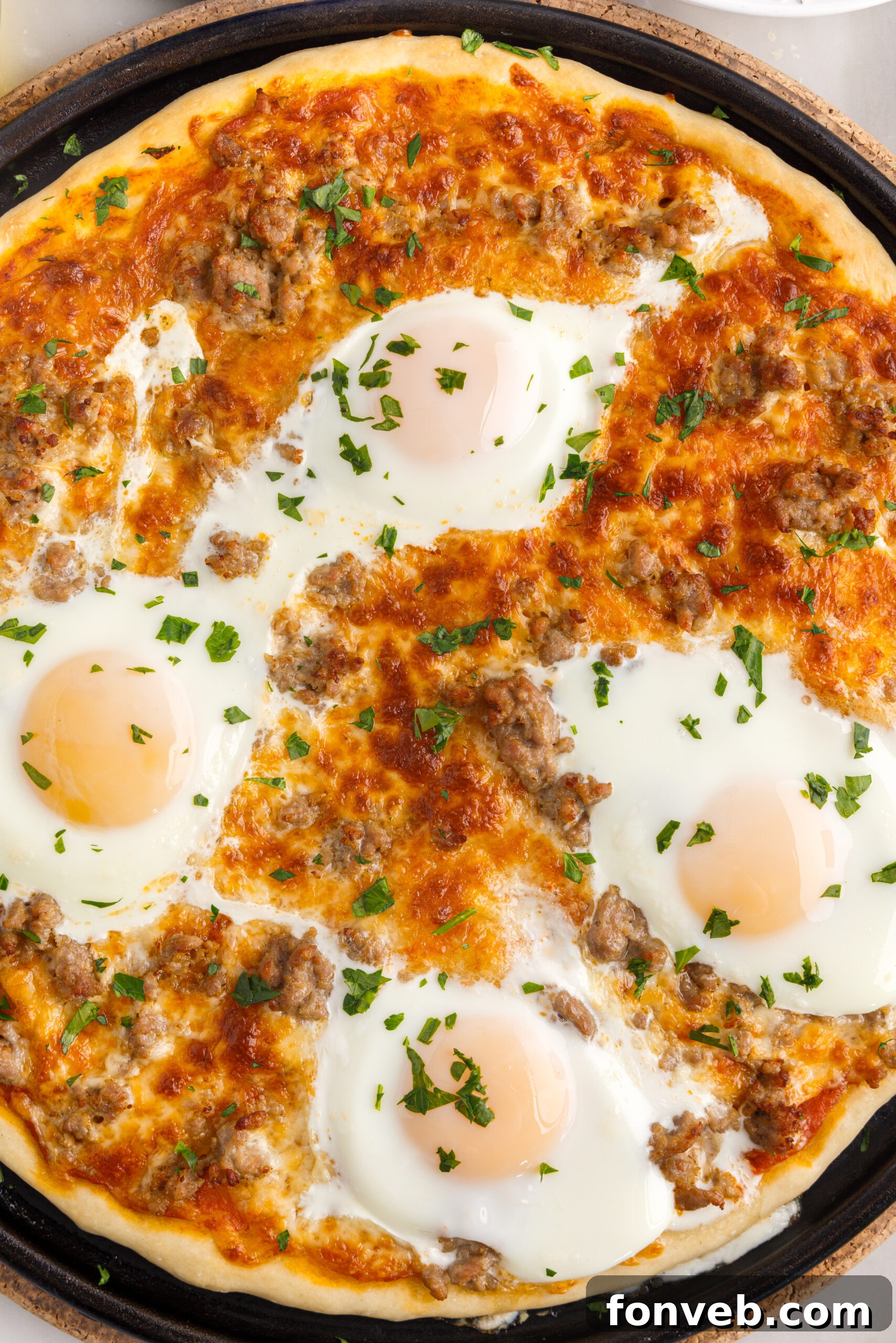 Close-up, overhead view of a freshly baked Breakfast Pizza, still hot on a black pizza pan, highlighting the golden crust and bubbling cheese.