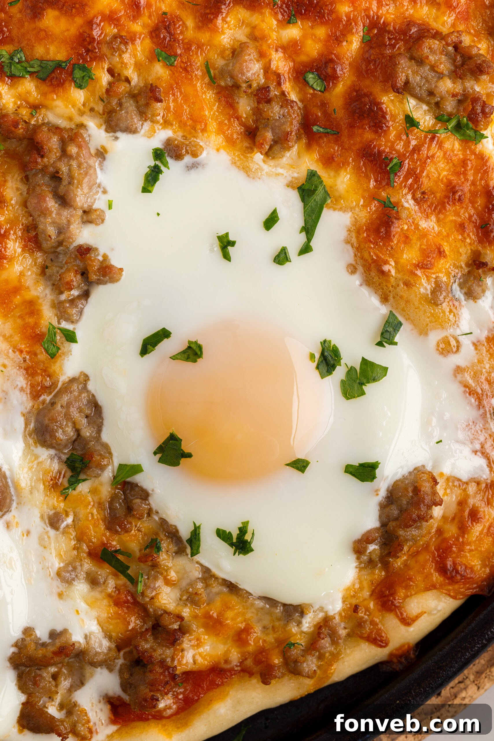 A close-up view of a slice of Breakfast Pizza, showing the perfectly cooked egg with a runny yolk, melted cheese, and bits of sausage on a crispy crust.
