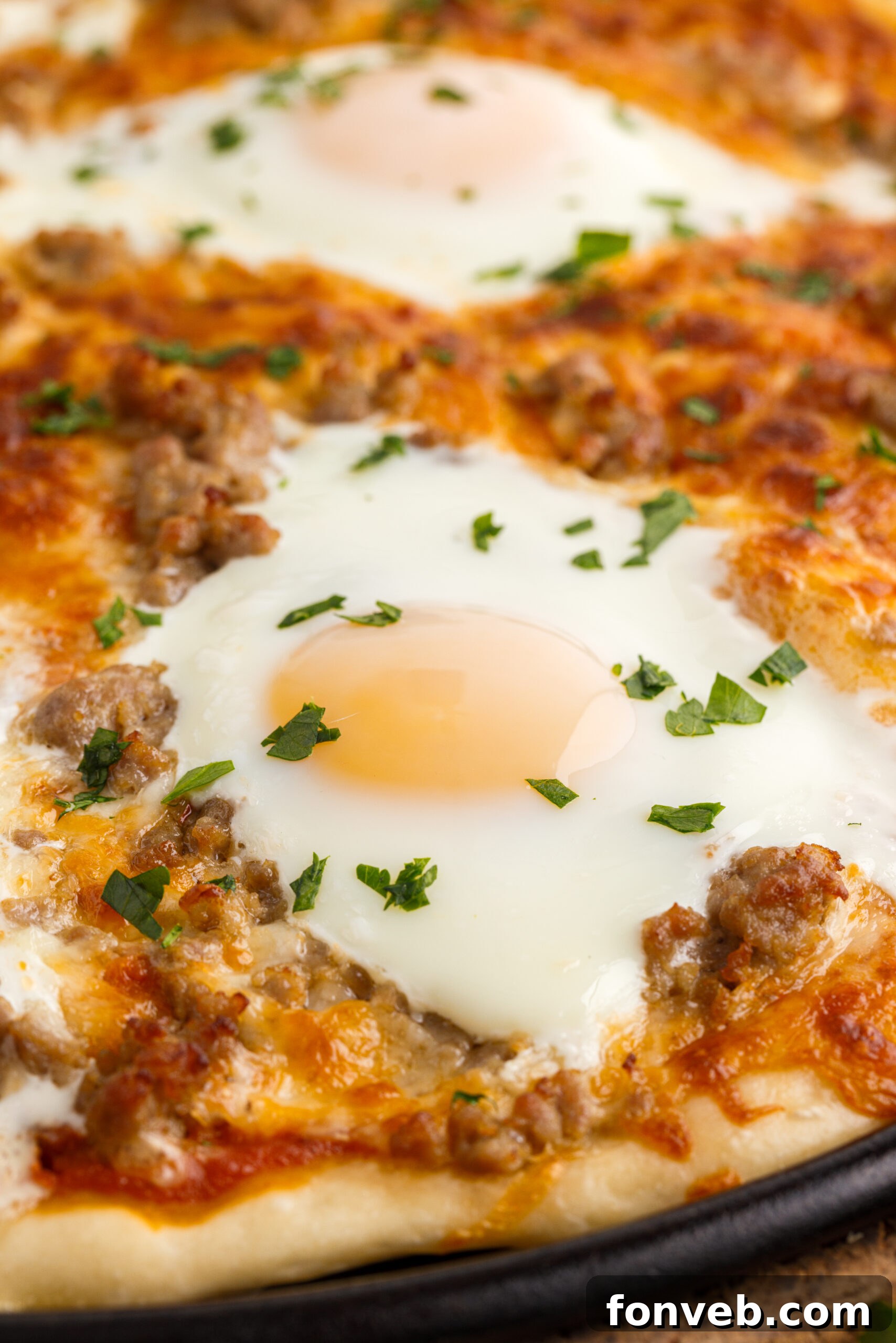 A tantalizing close-up of a golden-crusted Breakfast Pizza, rich with melted cheese, savory sausage, and perfectly cooked eggs, still on its black pizza pan.