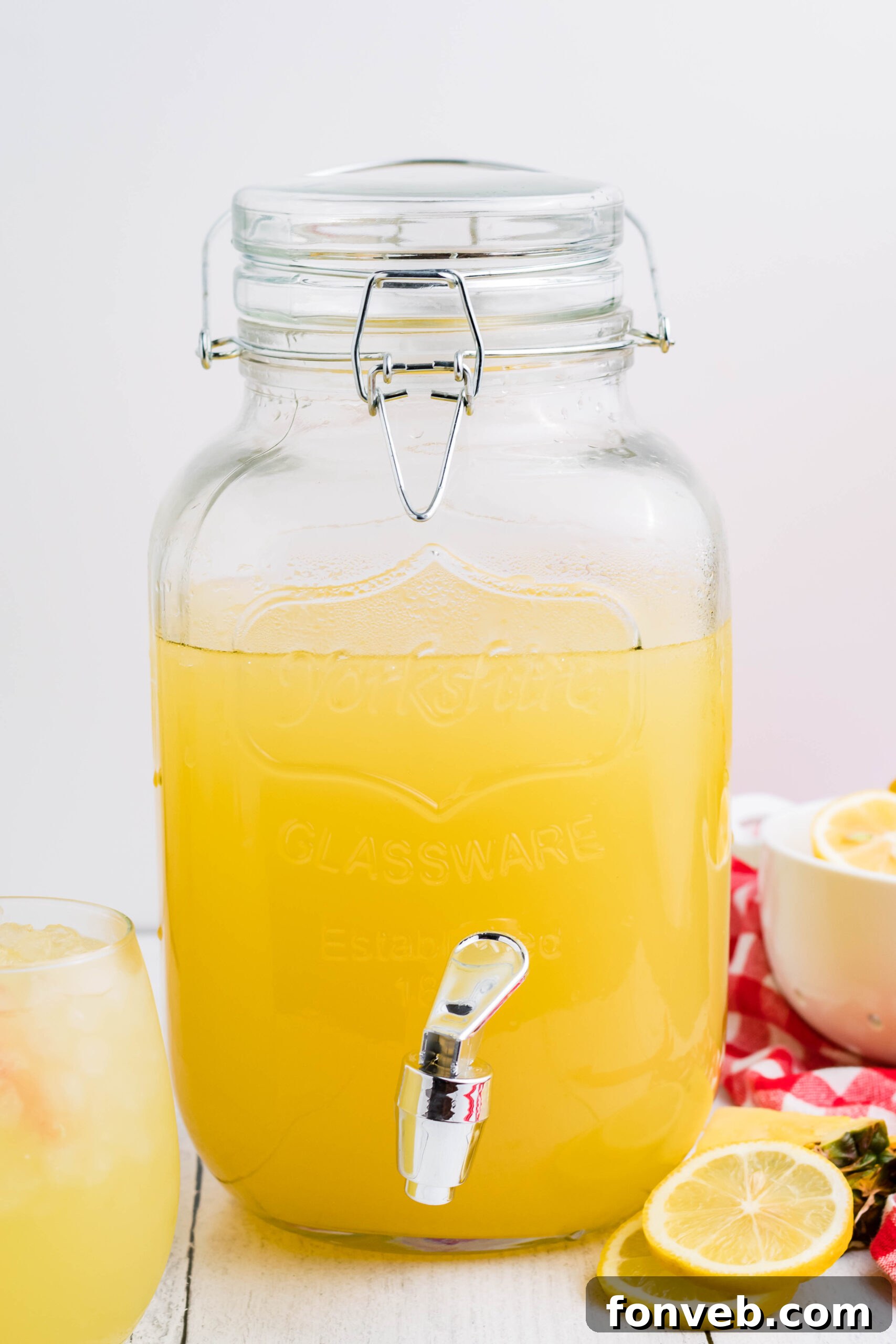 Front view of Pineapple Vodka Lemonade in a drink dispenser, garnished with fresh lemon and pineapple slices.