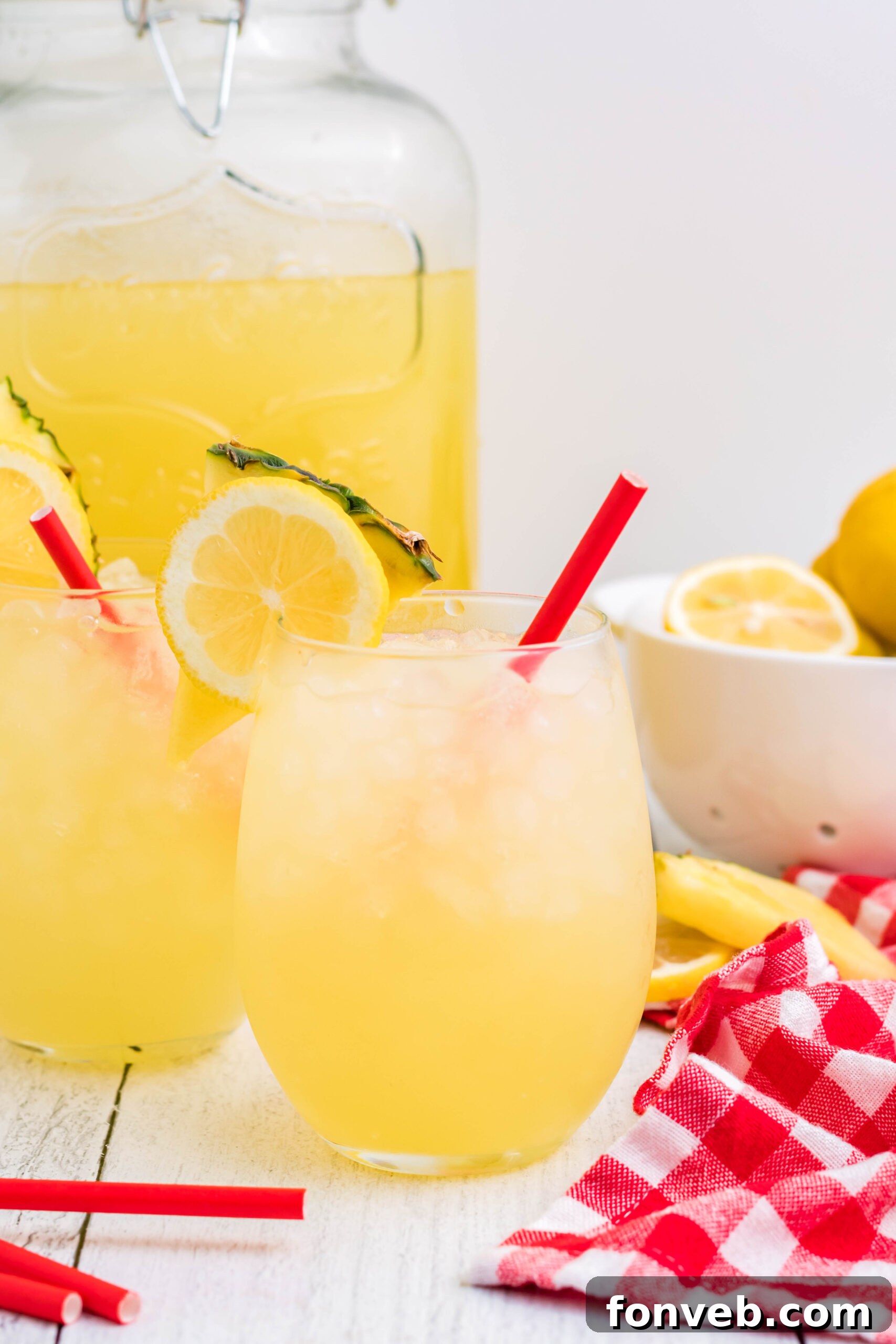 Front view of two glasses of Pineapple Vodka Lemonade garnished with a lemon and pineapple slice, ready to serve.