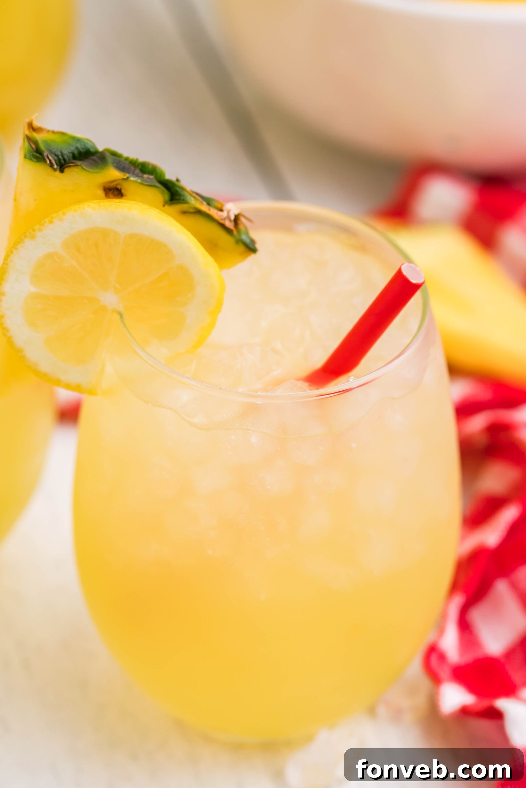 Close up view of two glasses of Pineapple Vodka Lemonade garnished with a lemon and pineapple slice, showing the vibrant color.