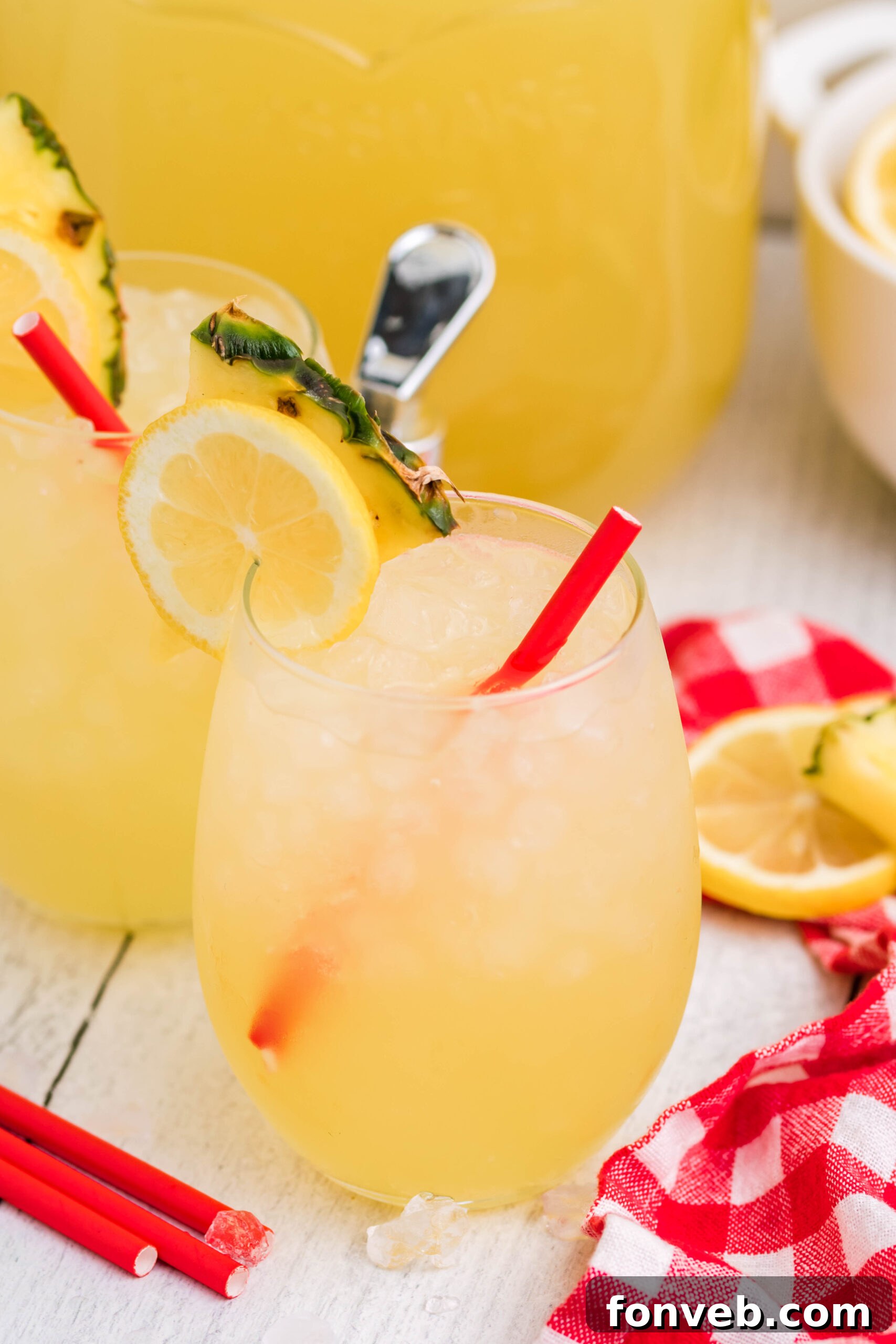 Front view of two glasses of Pineapple Vodka Lemonade garnished with a lemon and pineapple slice, sparkling with ice.
