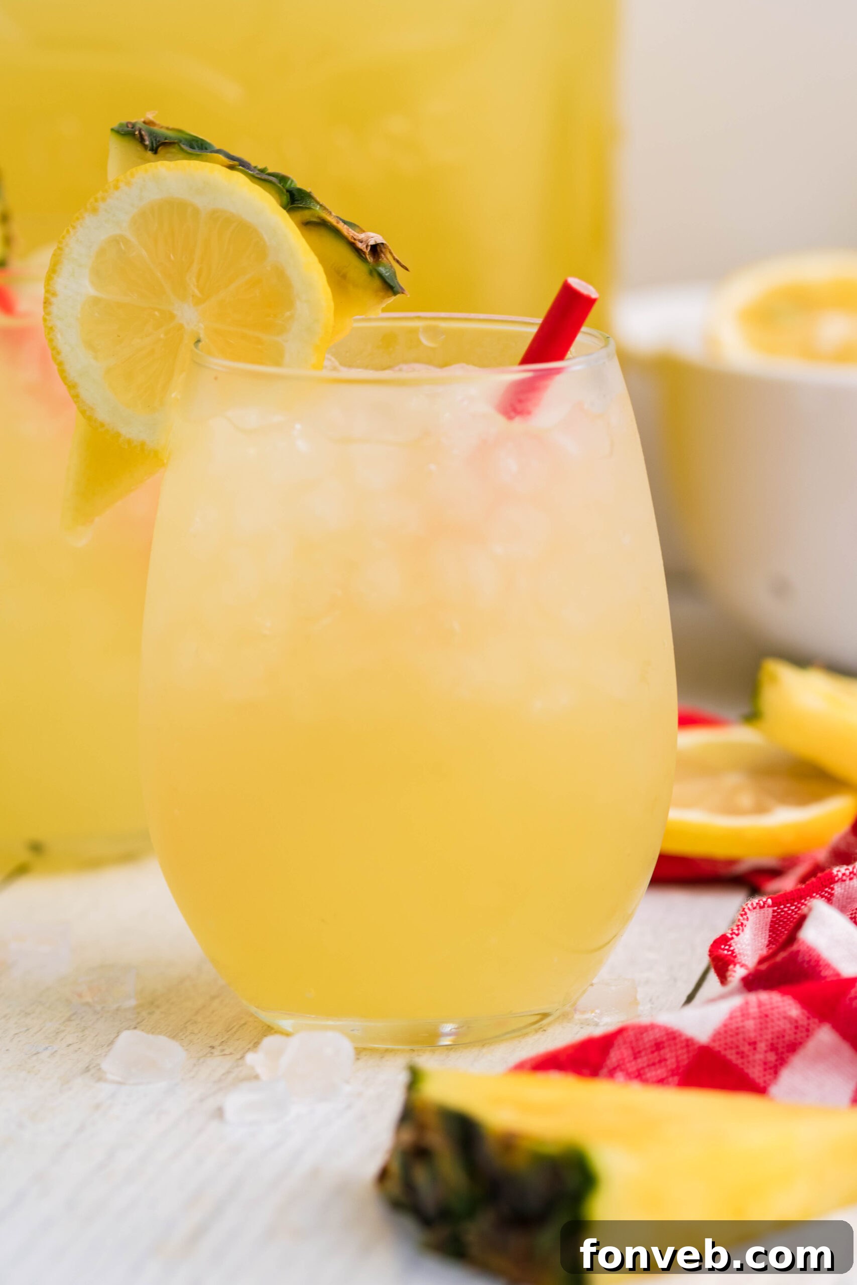 Front view of two glasses of Pineapple Vodka Lemonade garnished with a lemon and pineapple slice, glistening with condensation.