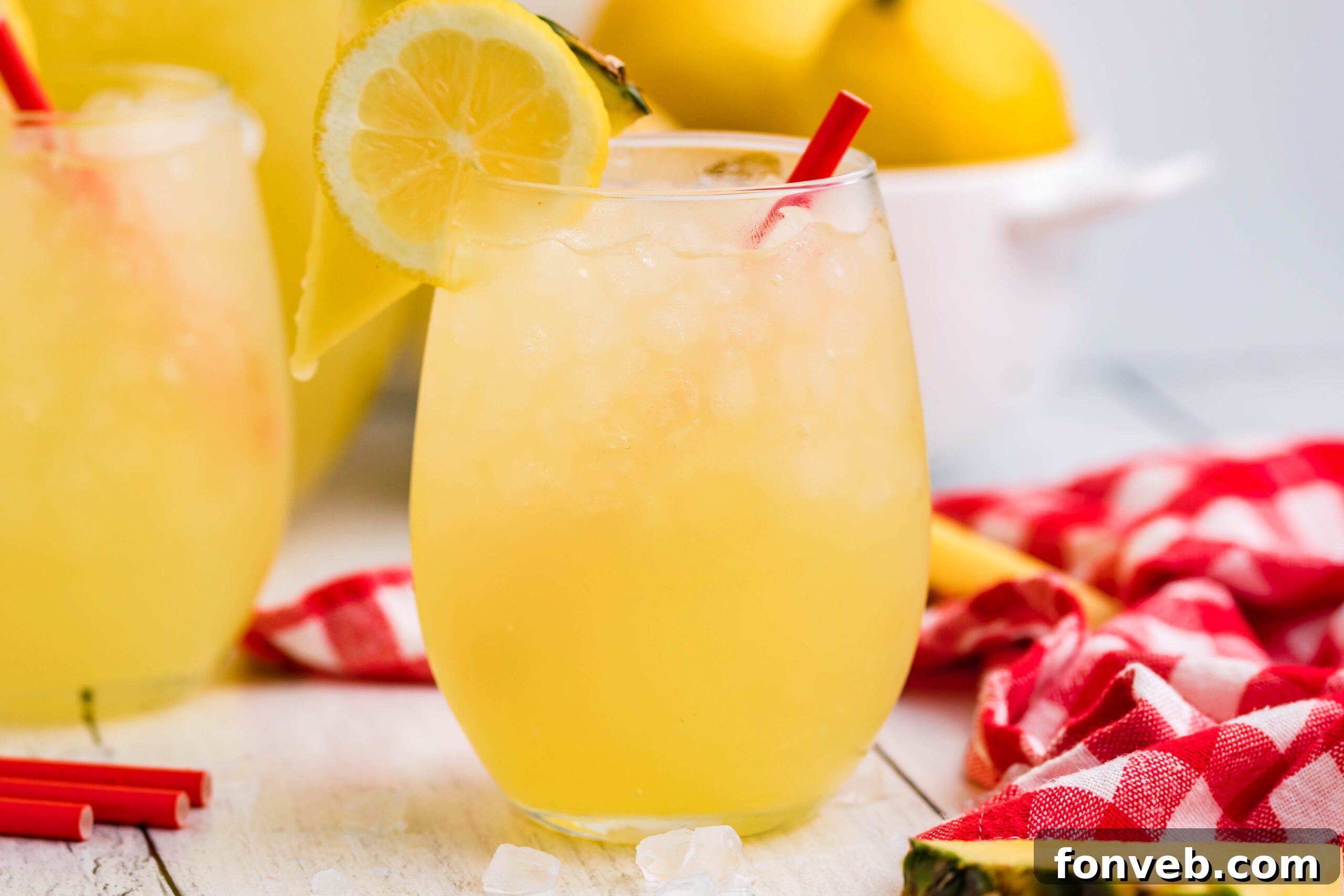 Front view of two glasses of Pineapple Vodka Lemonade garnished with a lemon and pineapple slice, on a light background.