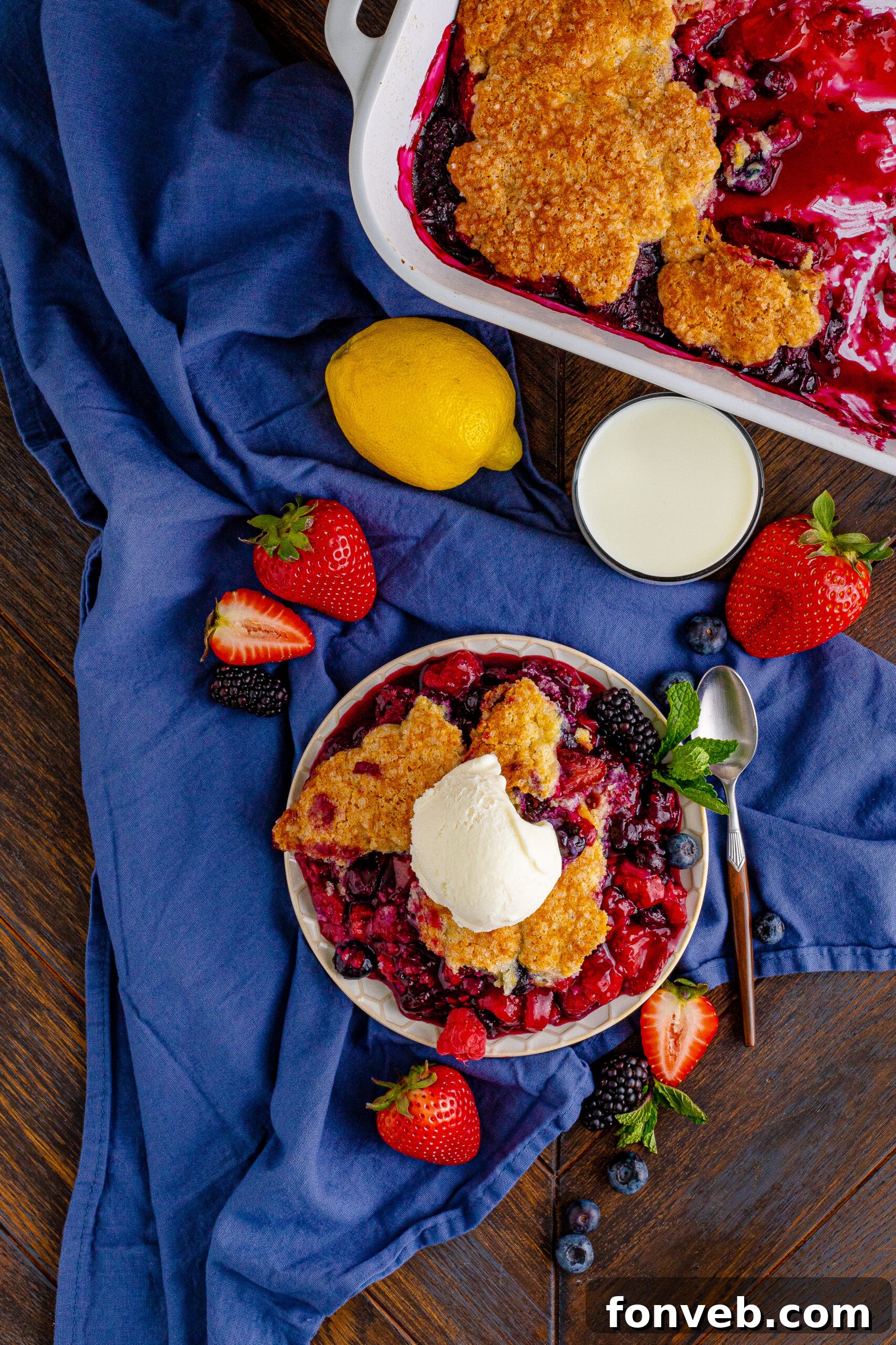 Overhead view of a perfectly baked Mixed Berry Cobbler, golden and bubbly, served on a white dish with a side of vanilla ice cream.