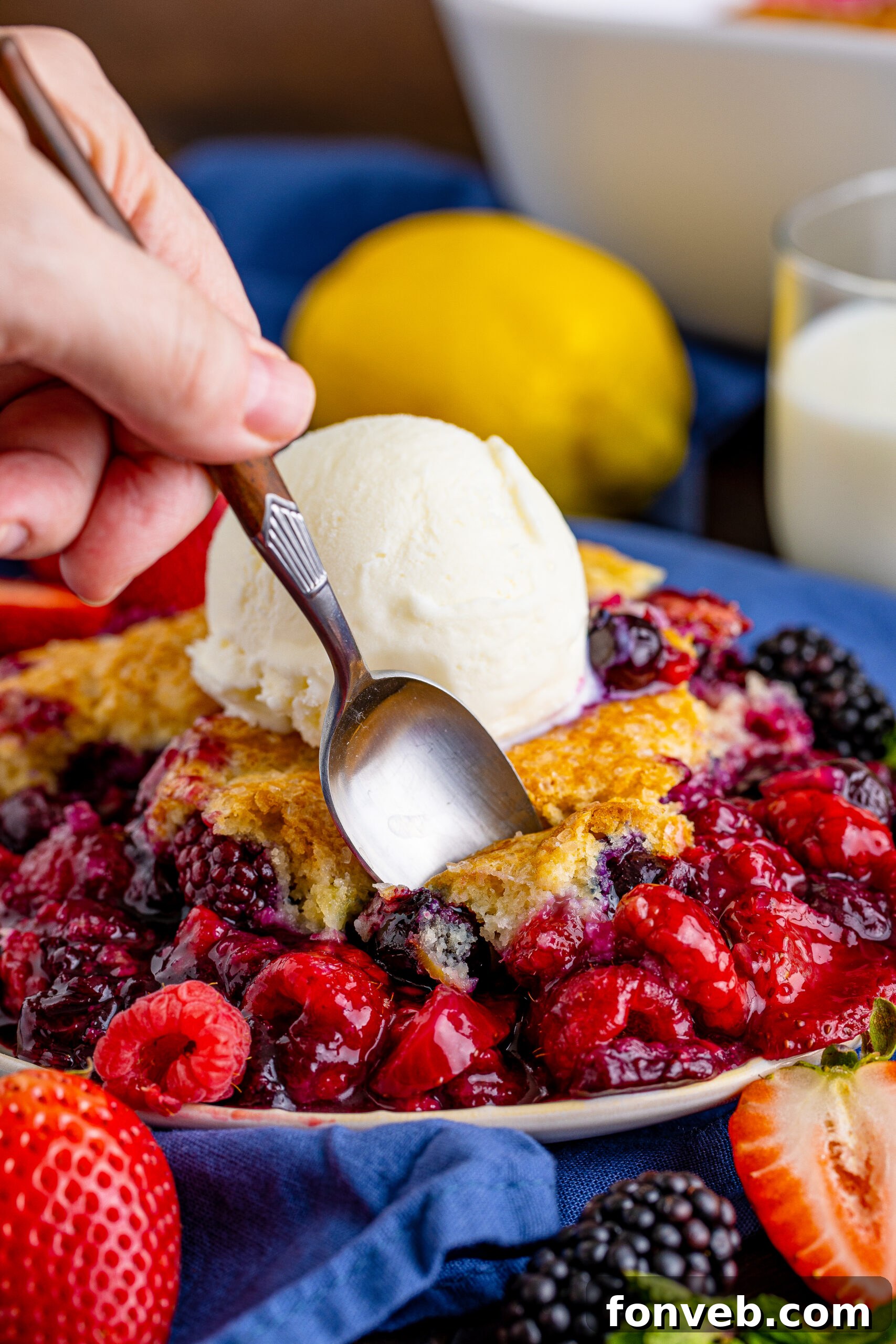 Front view of a Mixed Berry Cobbler on a white dish, with a silver spoon taking a perfect bite, showing the layers of fruit and crust.