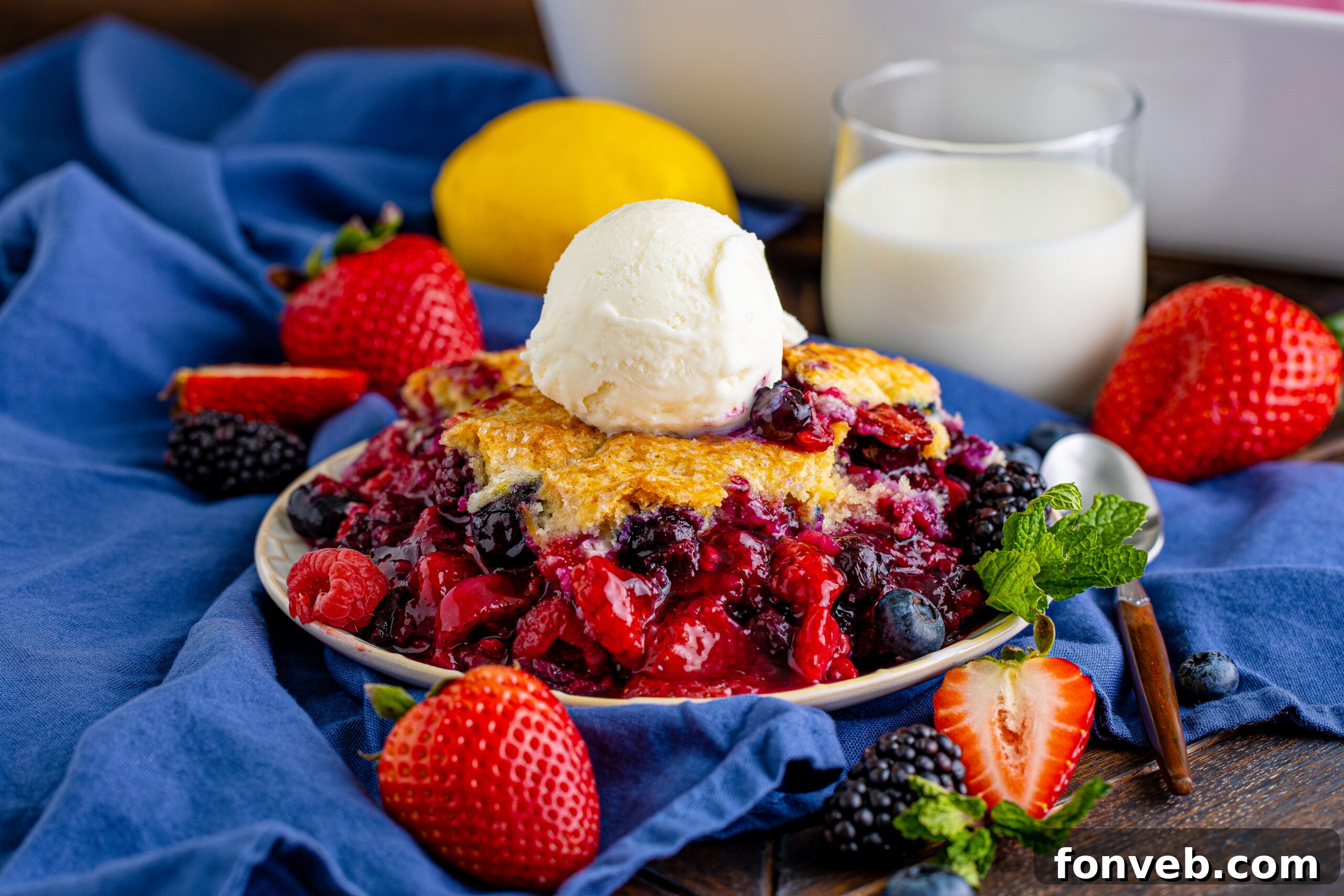 Front view of a whole Mixed Berry Cobbler in a white baking dish, ready to be served with a scoop of vanilla ice cream on the side.